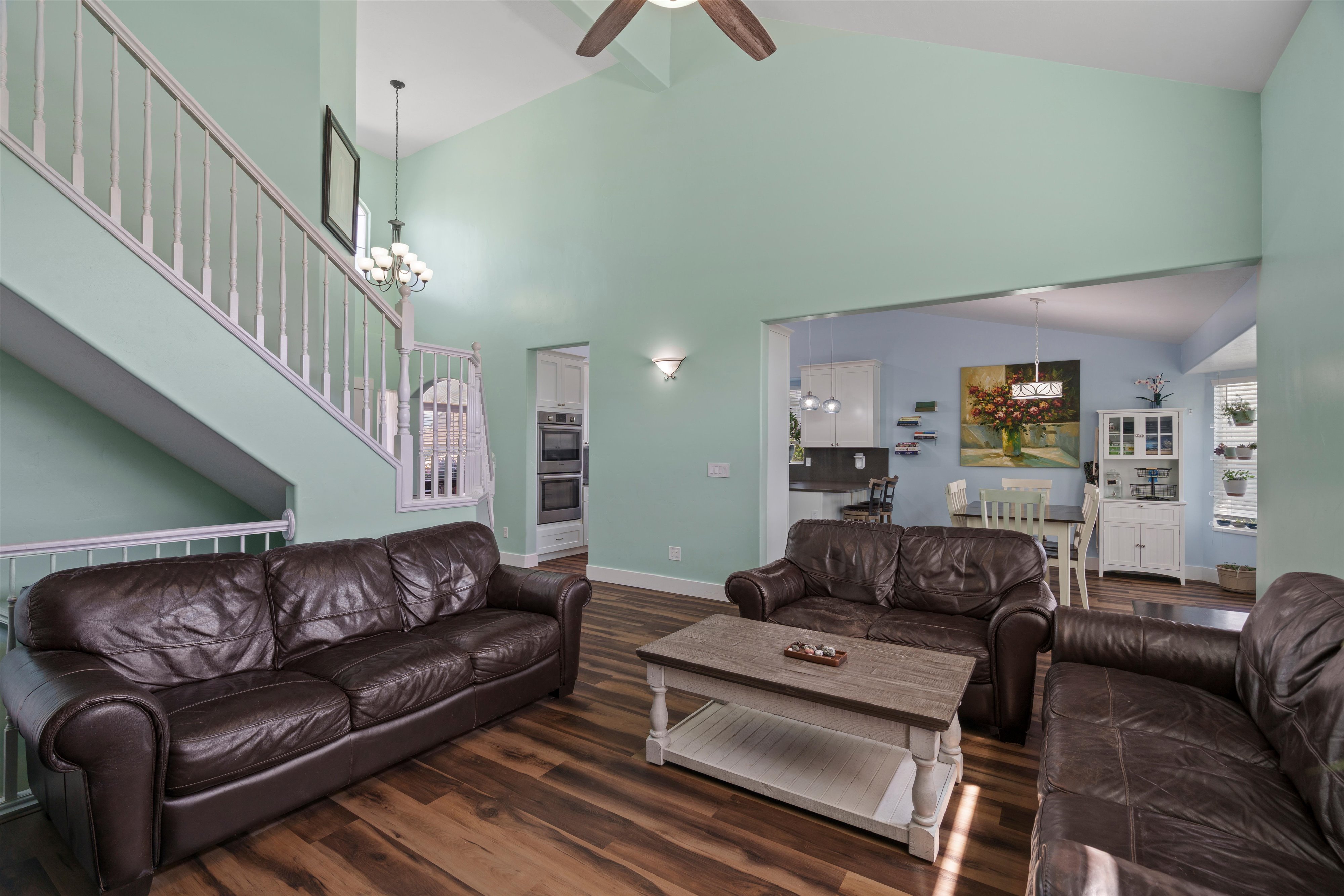 Vaulted ceiling living area with wood-finish flooring, staircase with white railing, and an opening to a dining area