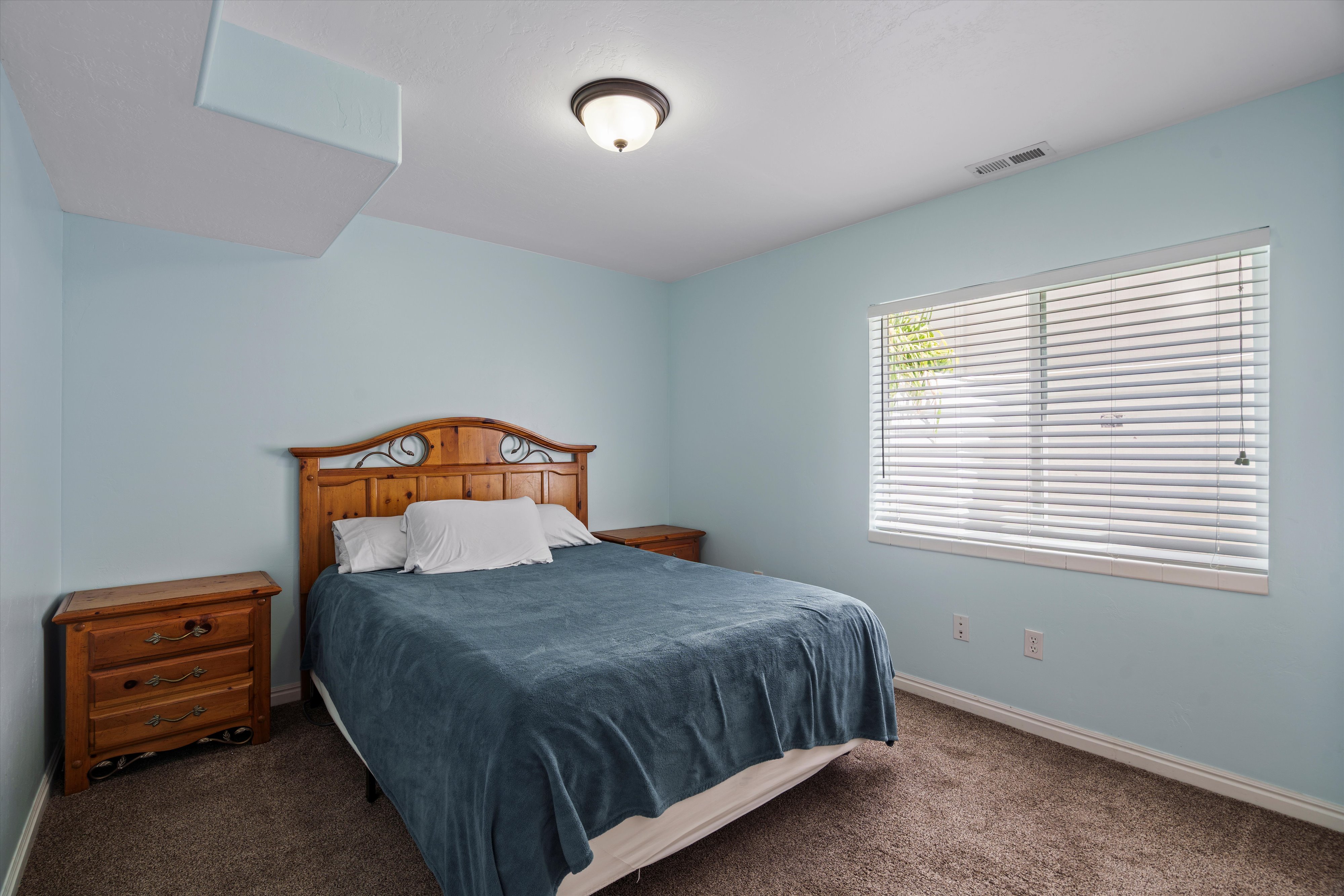 Carpeted bedroom featuring a single window with blinds, light blue walls, a white ceiling, and a flush mount light fixture