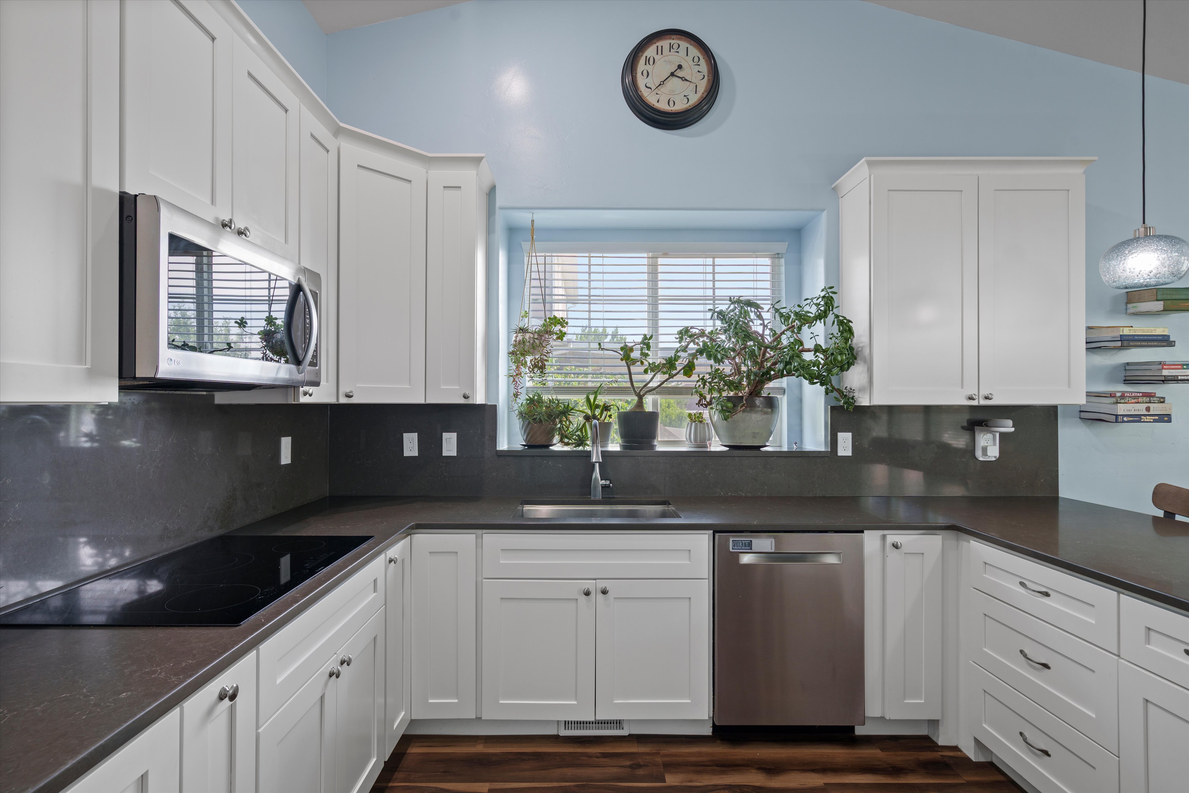 Modern kitchen featuring white shaker cabinetry, dark solid surface countertops, stainless steel appliances, and wood-finish flooring