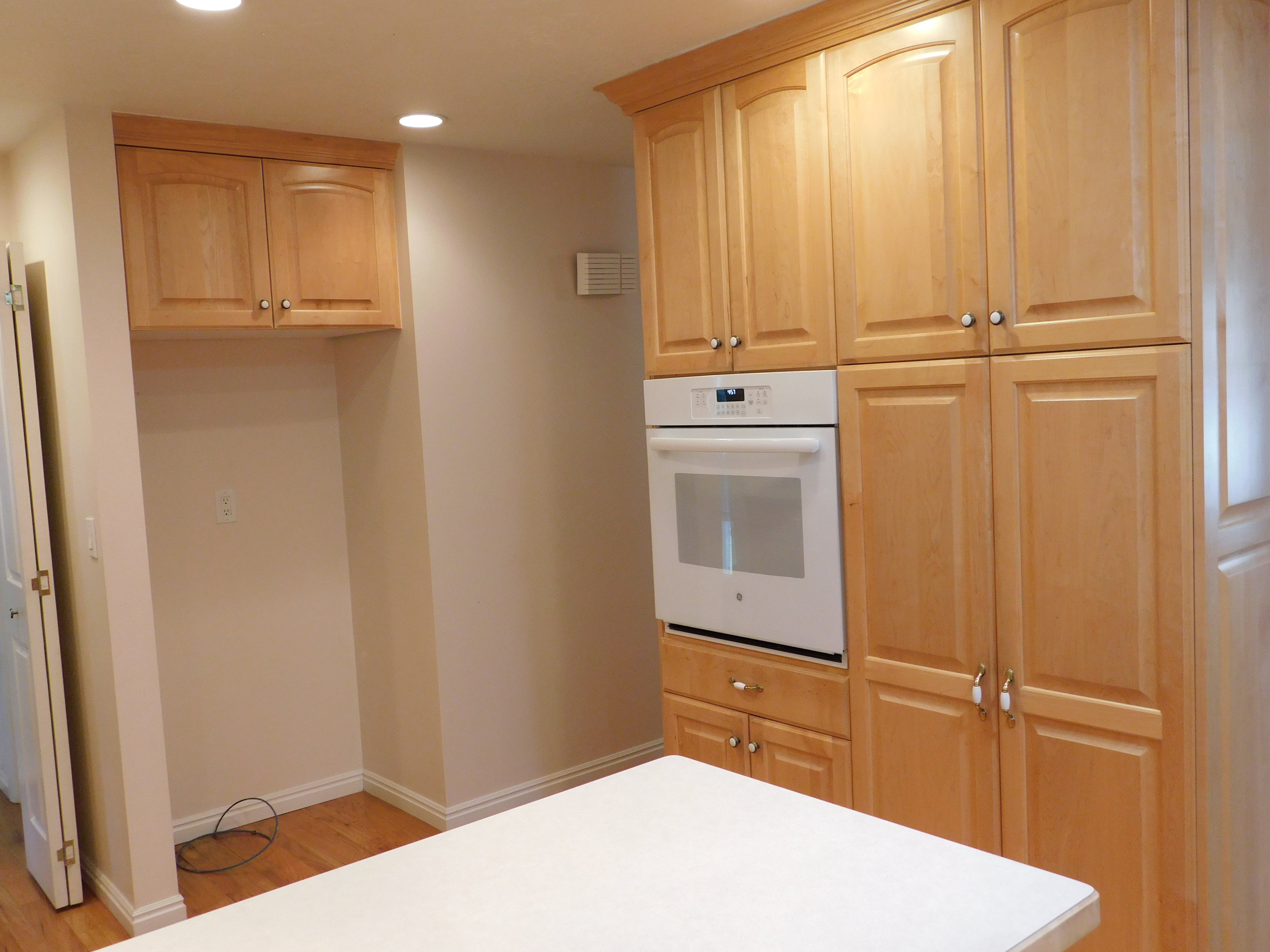 Kitchen featuring light wood cabinetry with crown molding, a built-in wall oven, recessed lighting, and wood-finish flooring