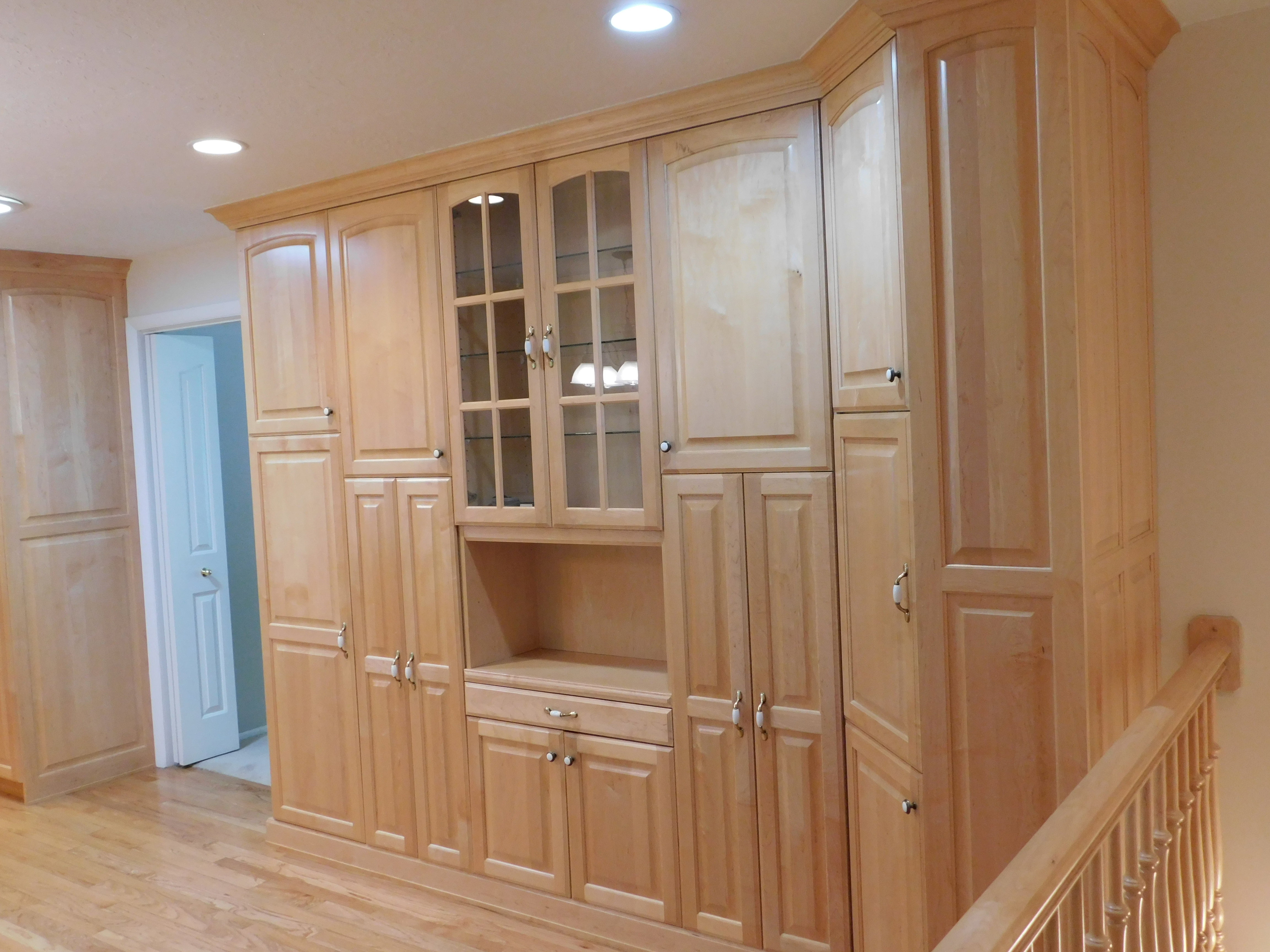Built-in cabinetry with glass-front display cabinets, light wood-finish flooring, recessed ceiling lighting, and a coordinating wood-finish stair railing