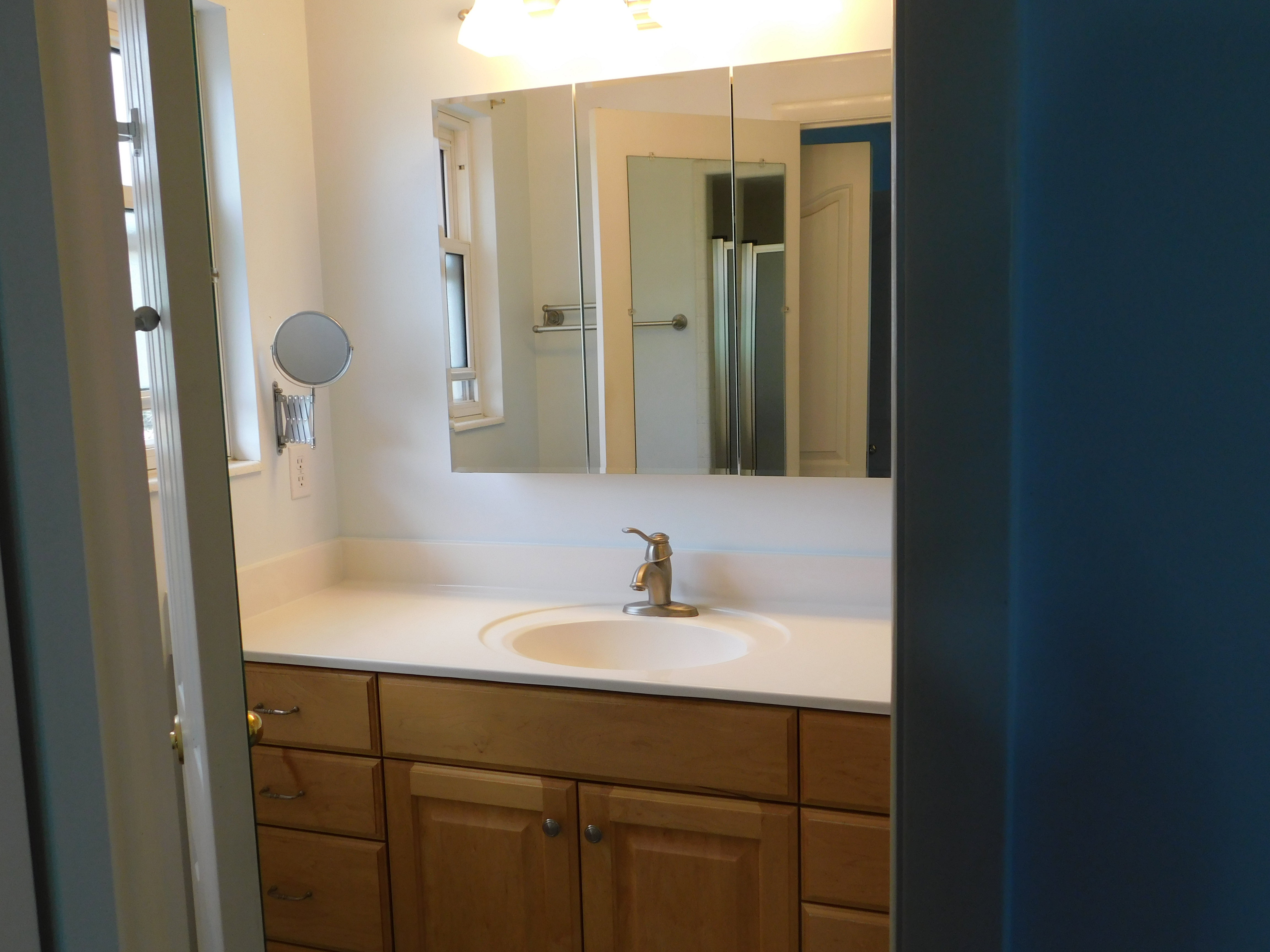 Vanity featuring a light wood-finish cabinet with brass hardware, a white countertop, and an undermount sink with a brass-finish faucet