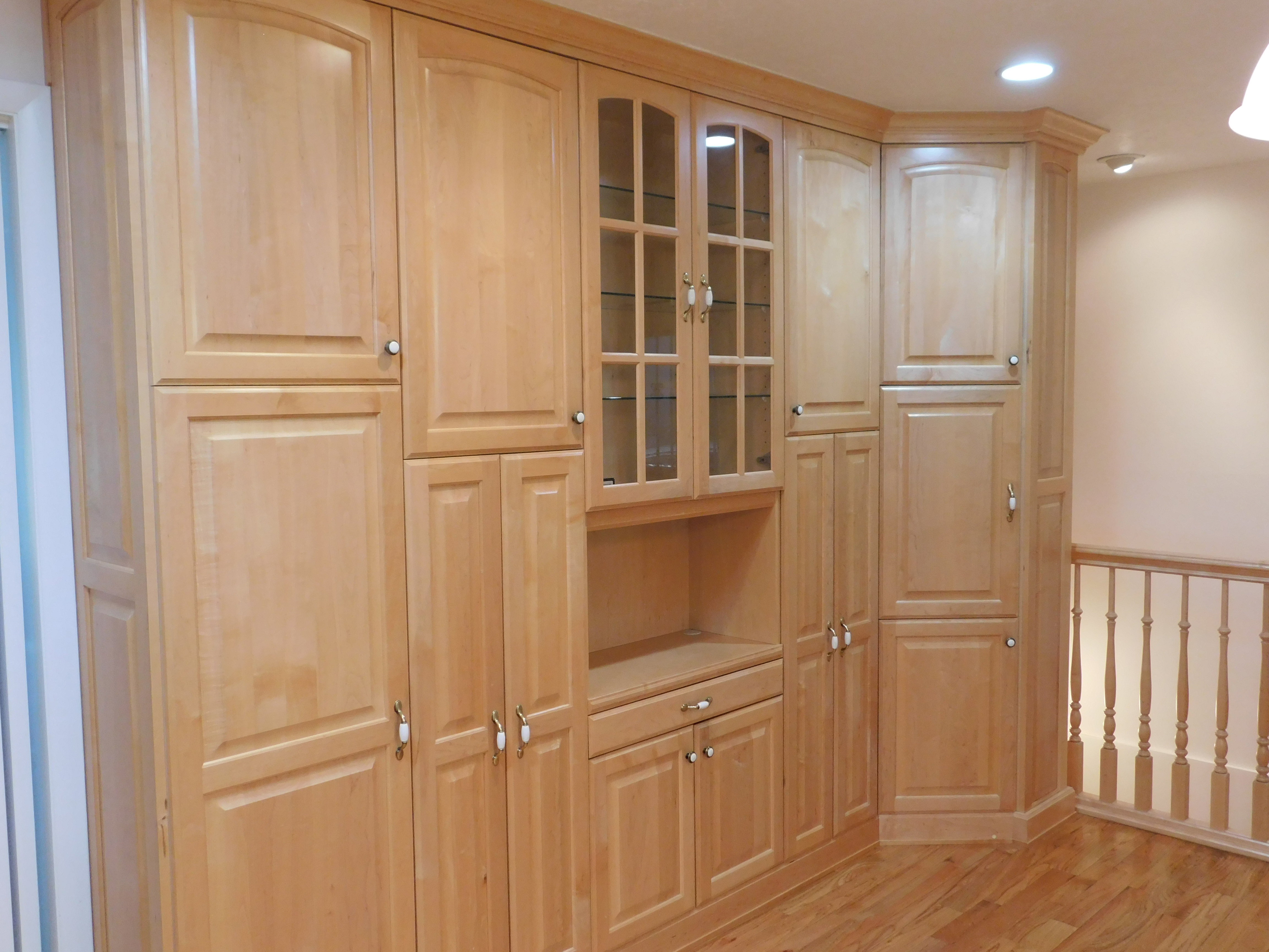 Built-in light wood cabinetry featuring glass-front display cabinets, various storage configurations, a recessed lighting fixture, and light wood-finish flooring