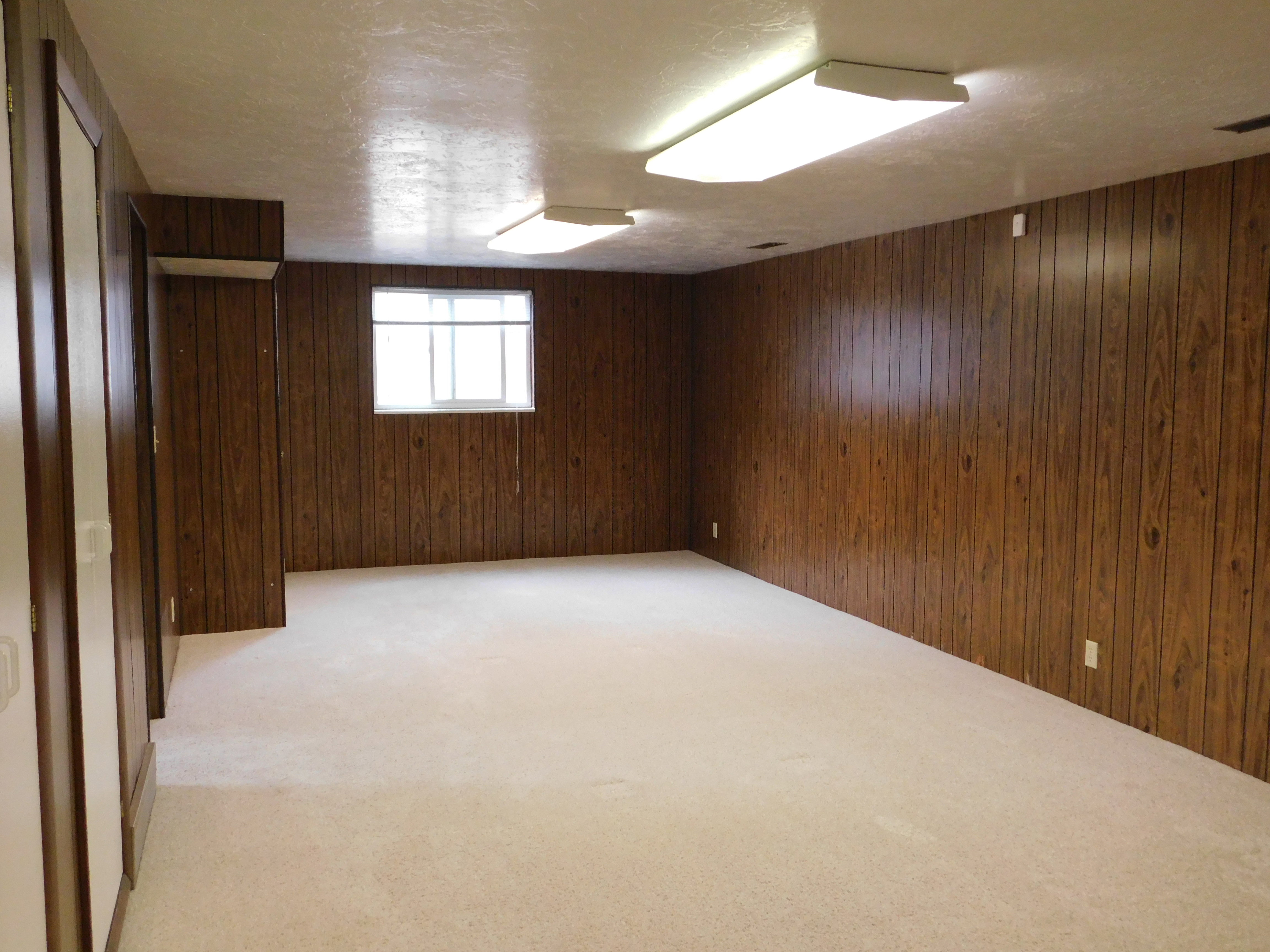 Spacious room featuring wood paneling walls and neutral-toned carpeting