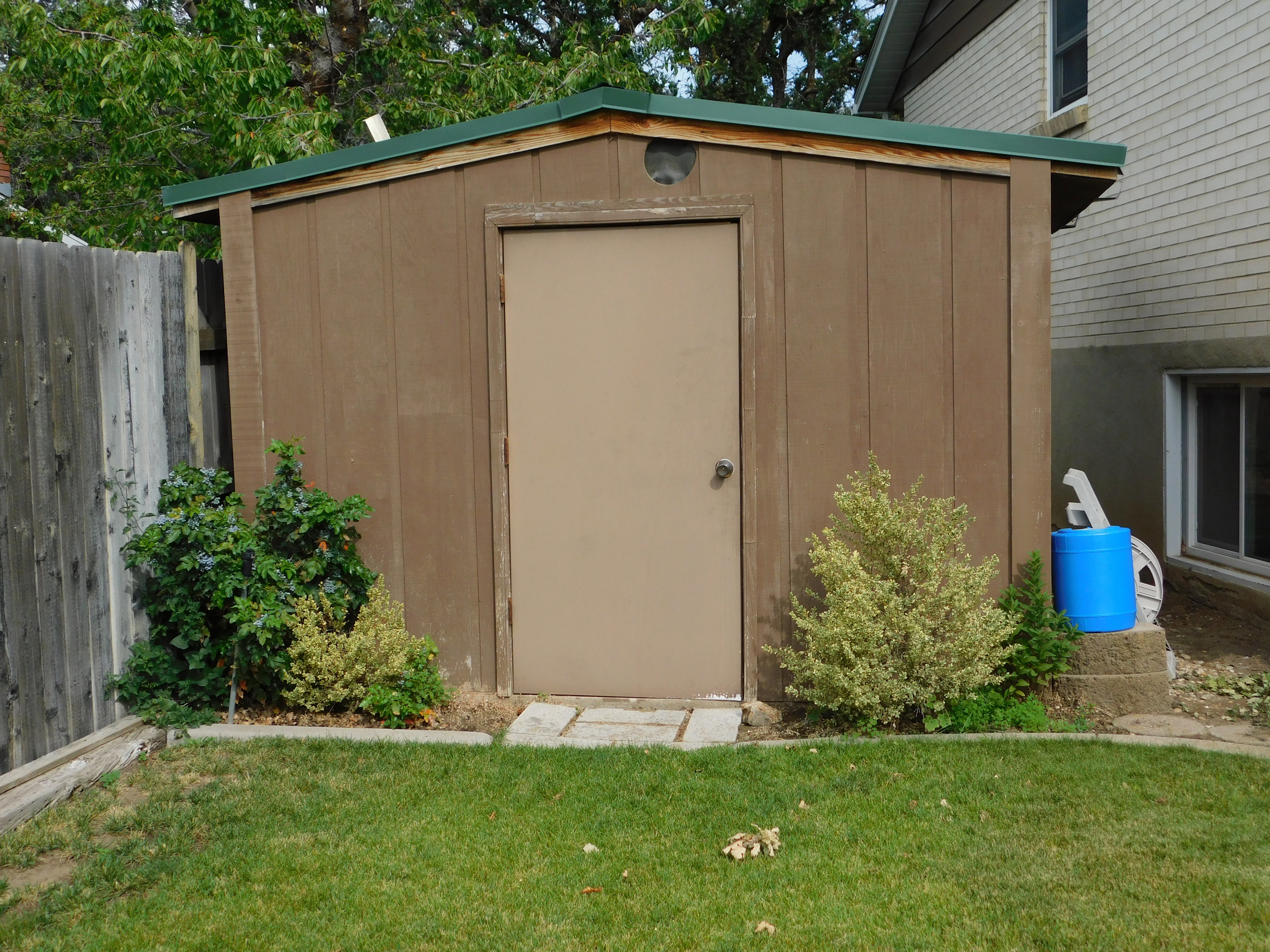 Freestanding storage shed with a brown wood-paneled exterior and a green roof