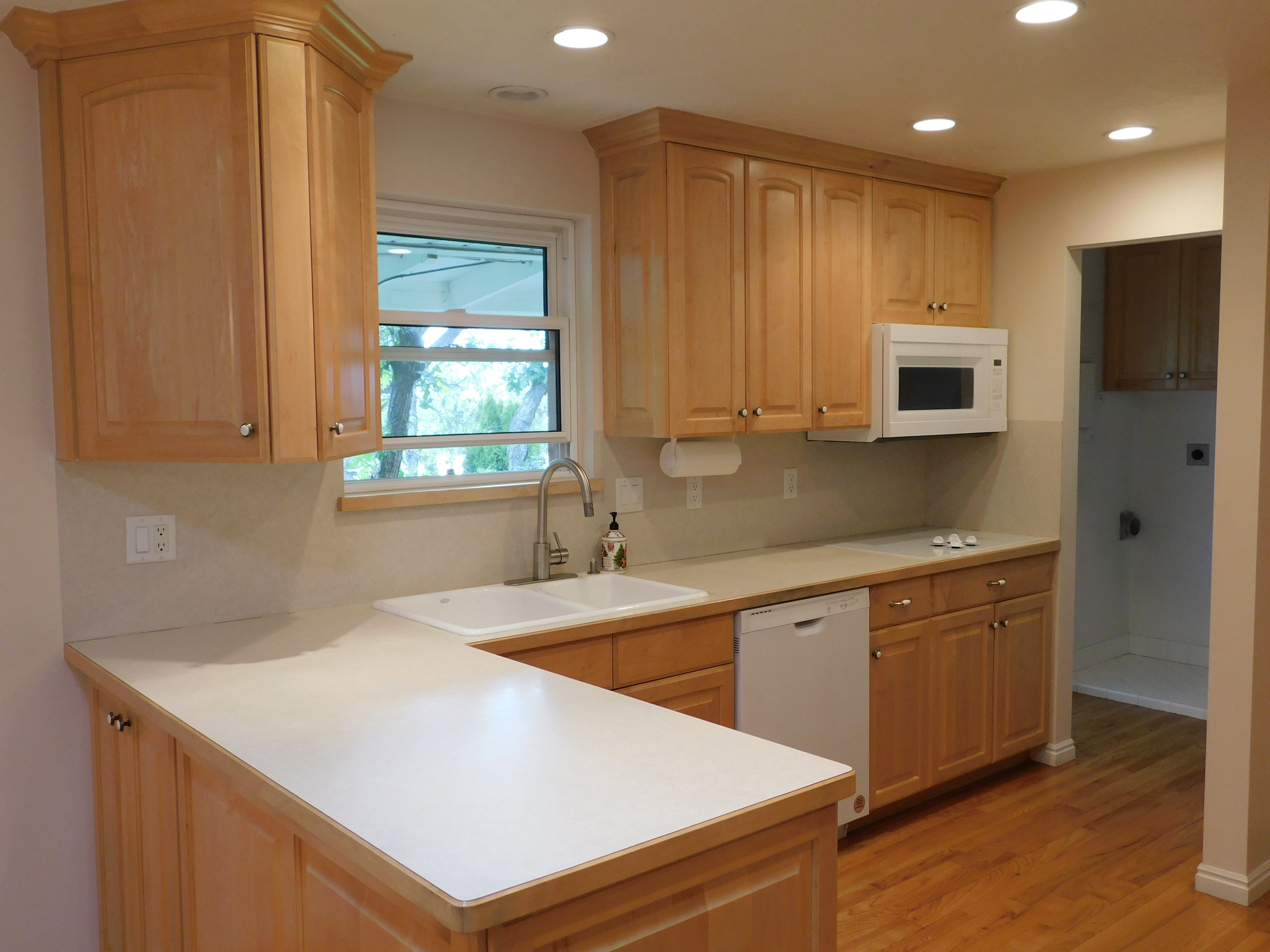 Kitchen featuring light wood cabinetry, recessed lighting, double basin sink with gooseneck faucet, light-toned countertops, and wood-finish flooring