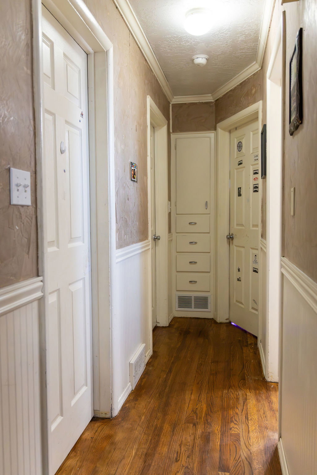 Hallway featuring wood-finish flooring, white paneled doors, wainscoting, built-in cabinetry with drawers, and crown molding