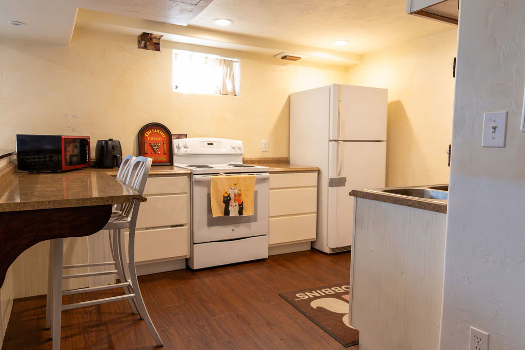 Compact kitchen featuring wood-finish flooring, white cabinetry, a built-in electric range, a refrigerator, and granite-look countertops