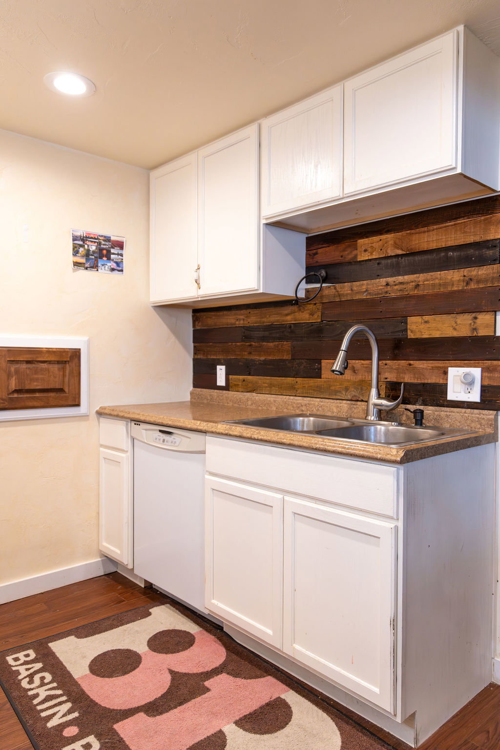 Kitchenette featuring a double basin stainless steel sink, white cabinetry, wood-finish flooring, a light-colored countertop, and a wood plank backsplash