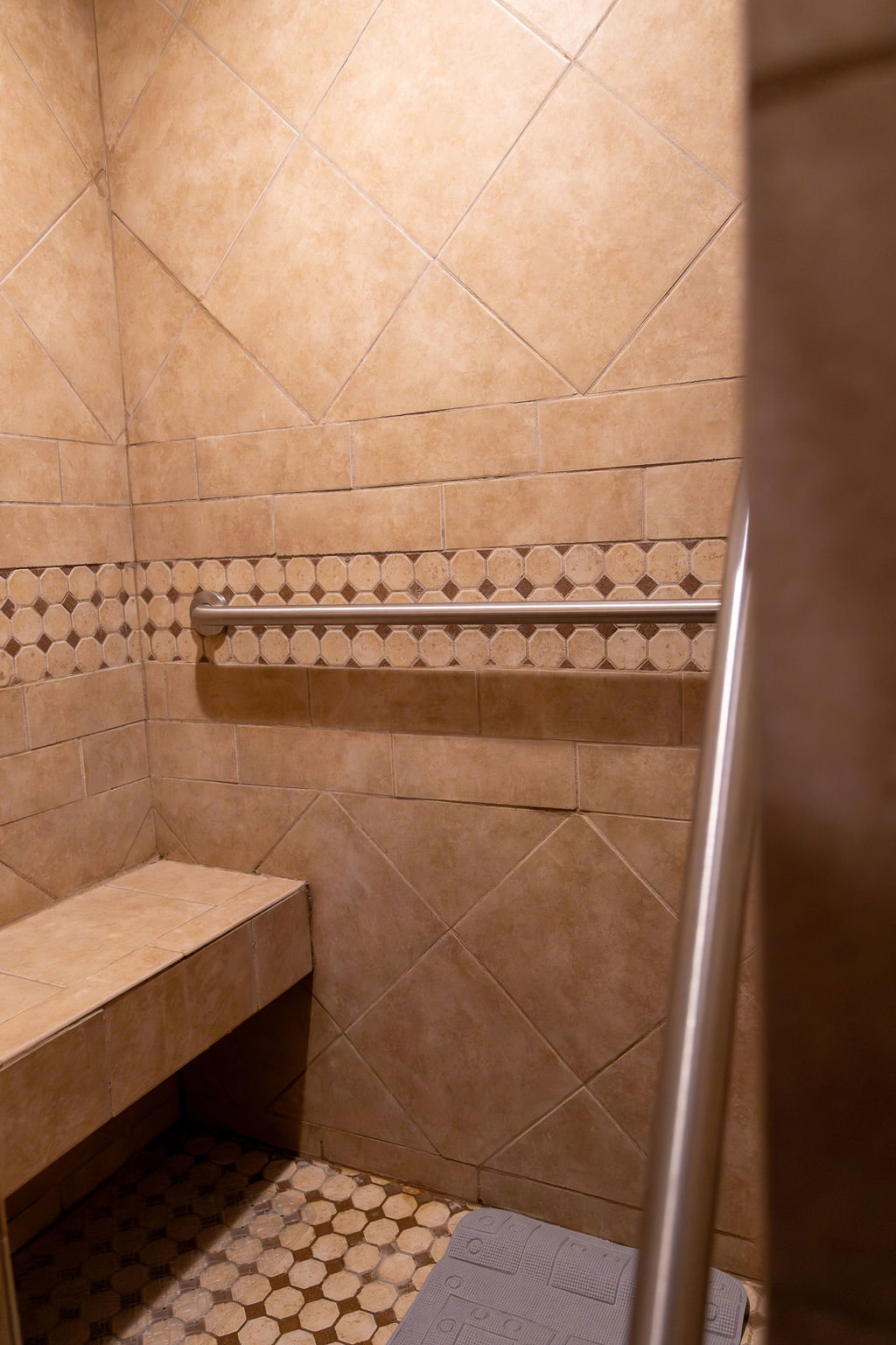 Tiled shower with a built-in bench, decorative accent tile band, and a metal grab bar
