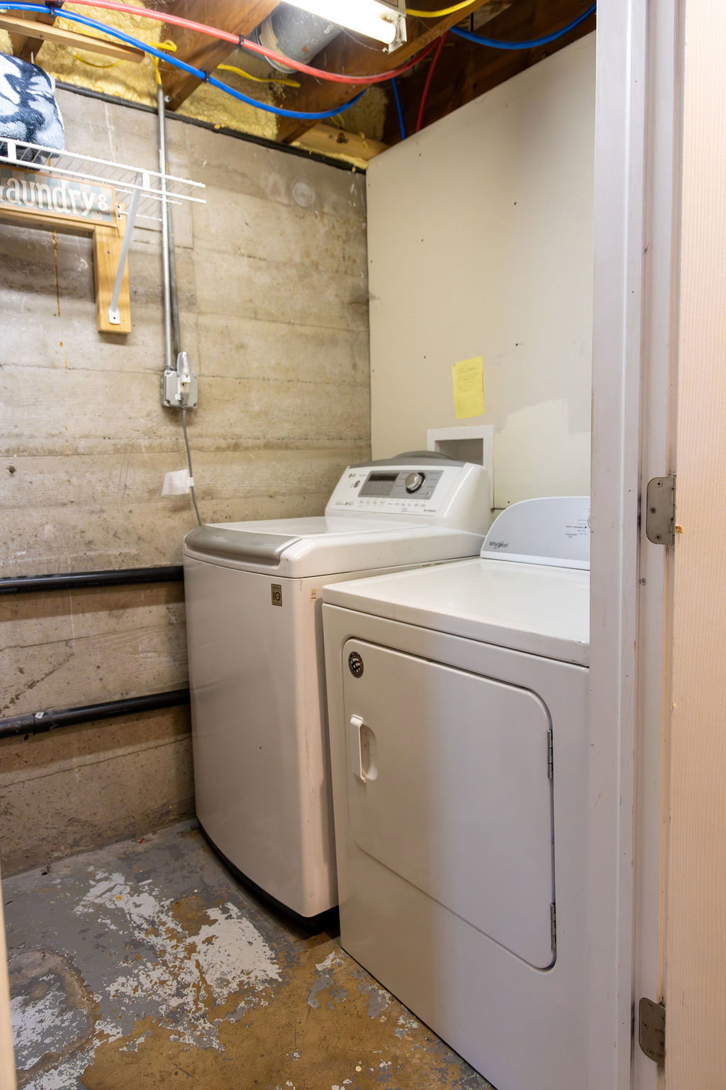 Dedicated laundry area featuring exposed concrete walls and ceiling joists