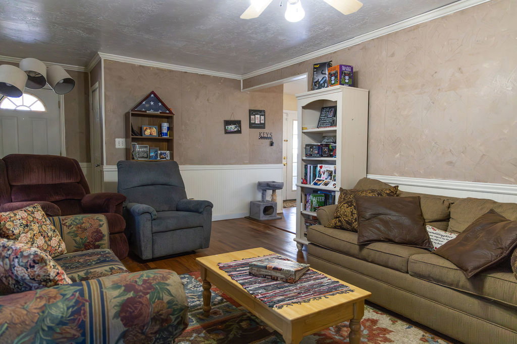 Warm living space featuring hardwood-finish flooring, a ceiling fan with light fixture, decorative wall paneling, and a built-in shelving unit