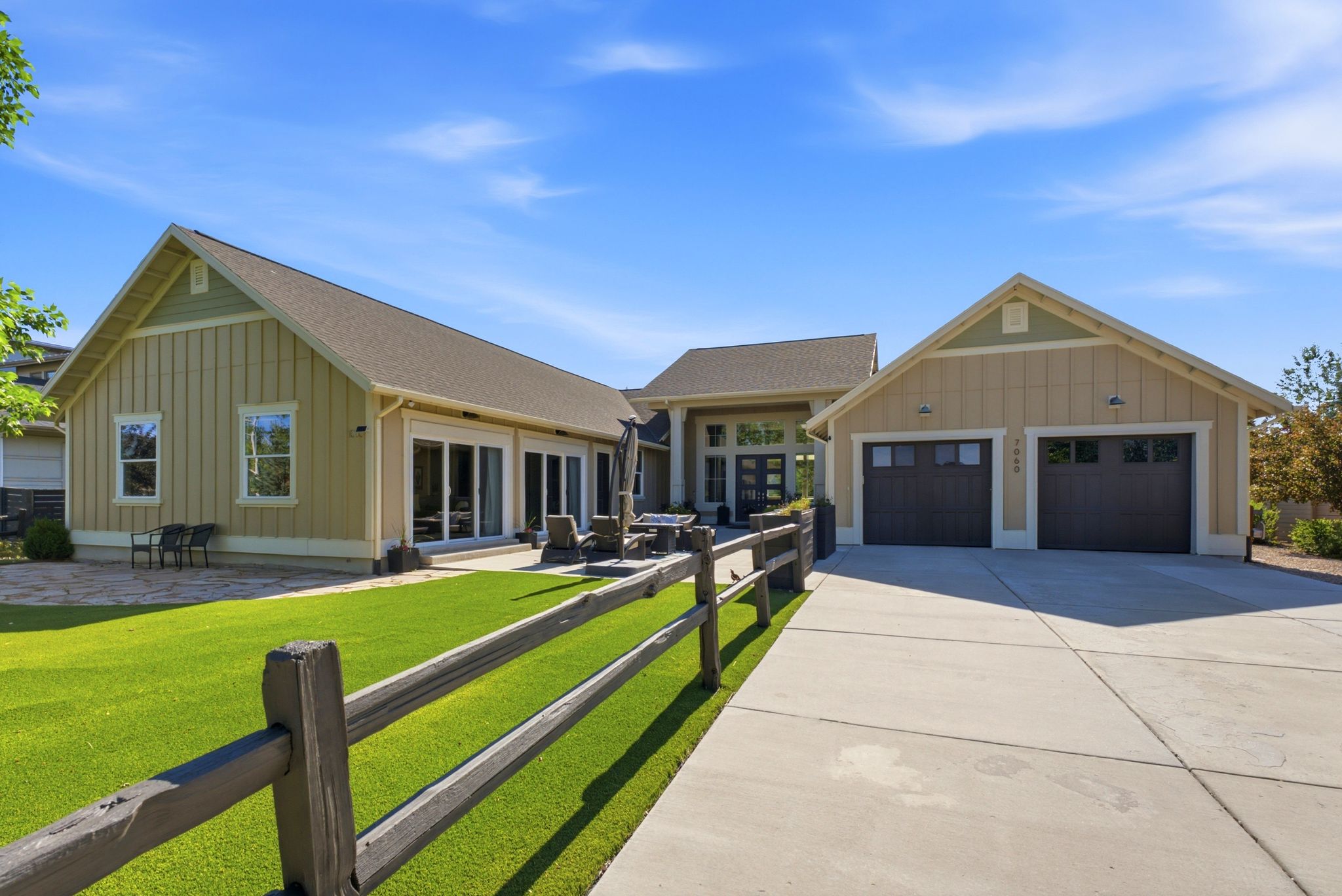 Contemporary exterior with board and batten siding, a two-car garage with carriage-style doors, a concrete driveway, and a fenced artificial turf lawn