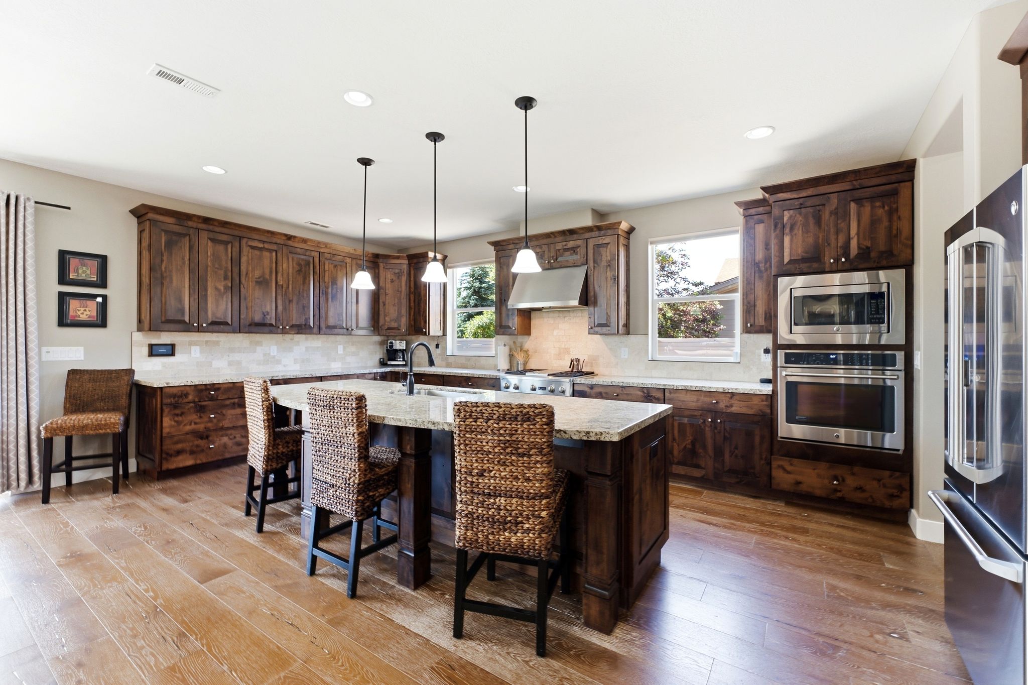 Spacious kitchen featuring rich wood cabinetry, stainless steel appliances, a large central island with seating, pendant lighting, and wood-finish flooring