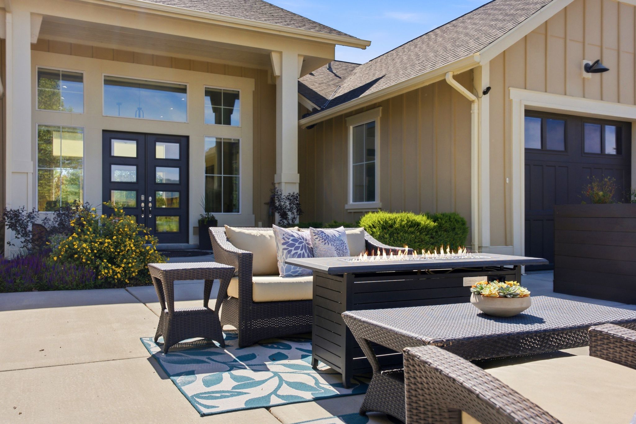 Entryway patio featuring a built-in fire pit, board-and-batten siding, a dark paneled garage door, and a double-door entry with transom and side windows