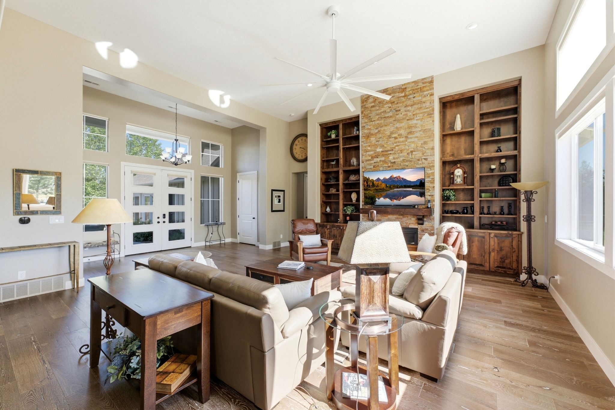 Spacious living area featuring wood-finish flooring, a stone accent wall with a fireplace, and built-in shelving