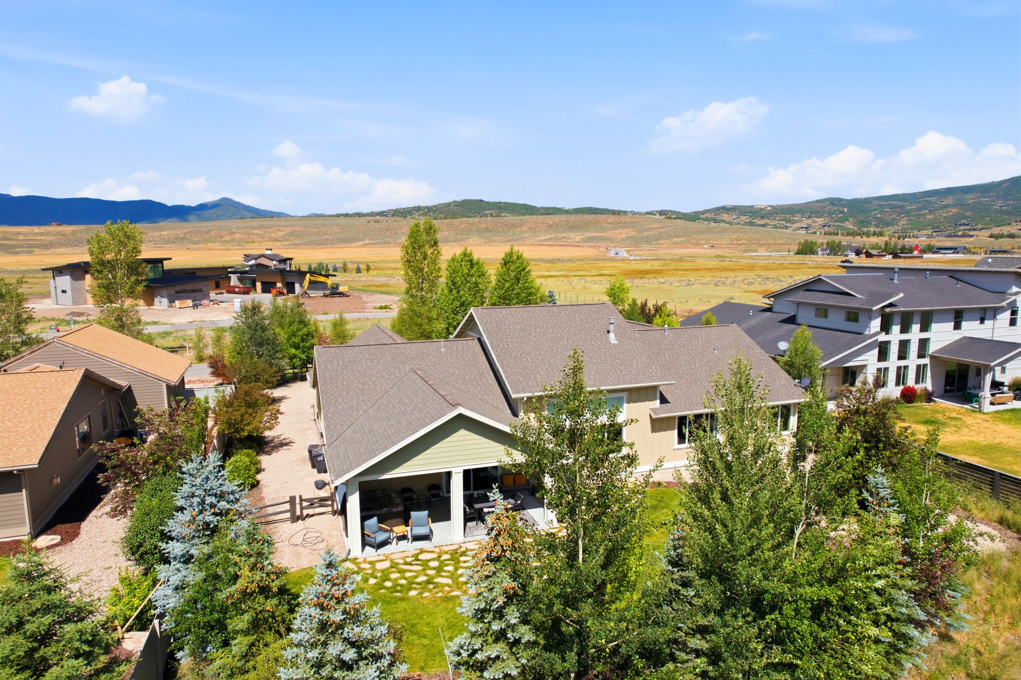 Expansive property featuring a covered patio, stone paver patio, lush green lawn, mature trees, and a mountain backdrop
