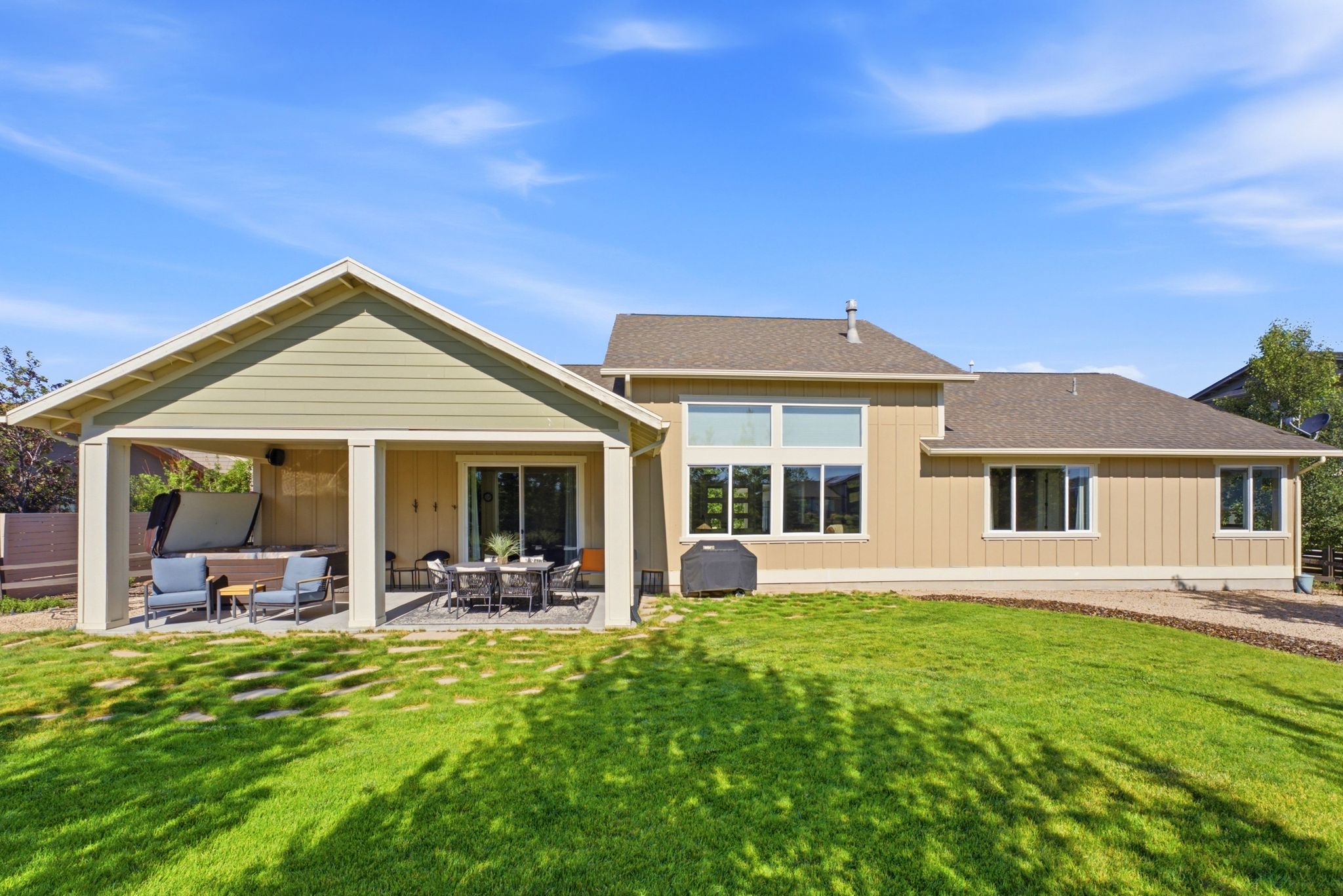 Expansive rear exterior featuring a covered patio with recessed lighting, a sliding glass door, a large turf lawn, and multiple windows