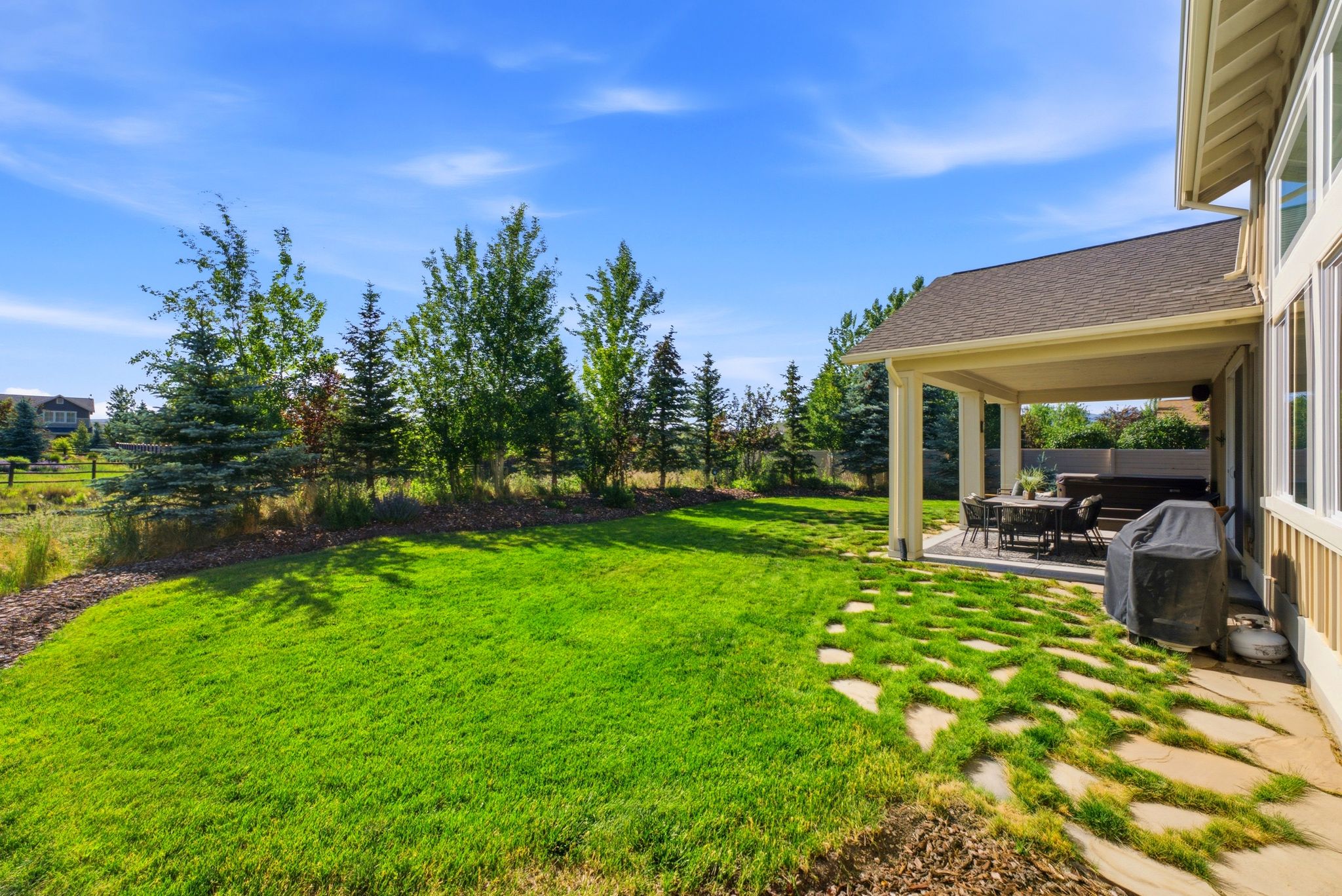 Expansive lawn area featuring a covered patio, stone paver pathway, and mature tree landscaping