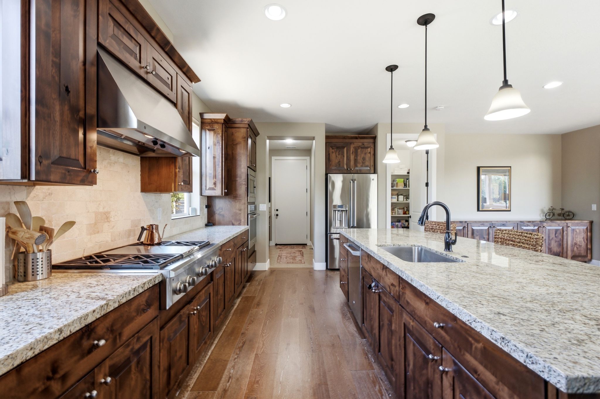 Kitchen featuring wood-finish flooring, dark wood cabinetry, light speckled countertops, stainless steel appliances, and recessed lighting