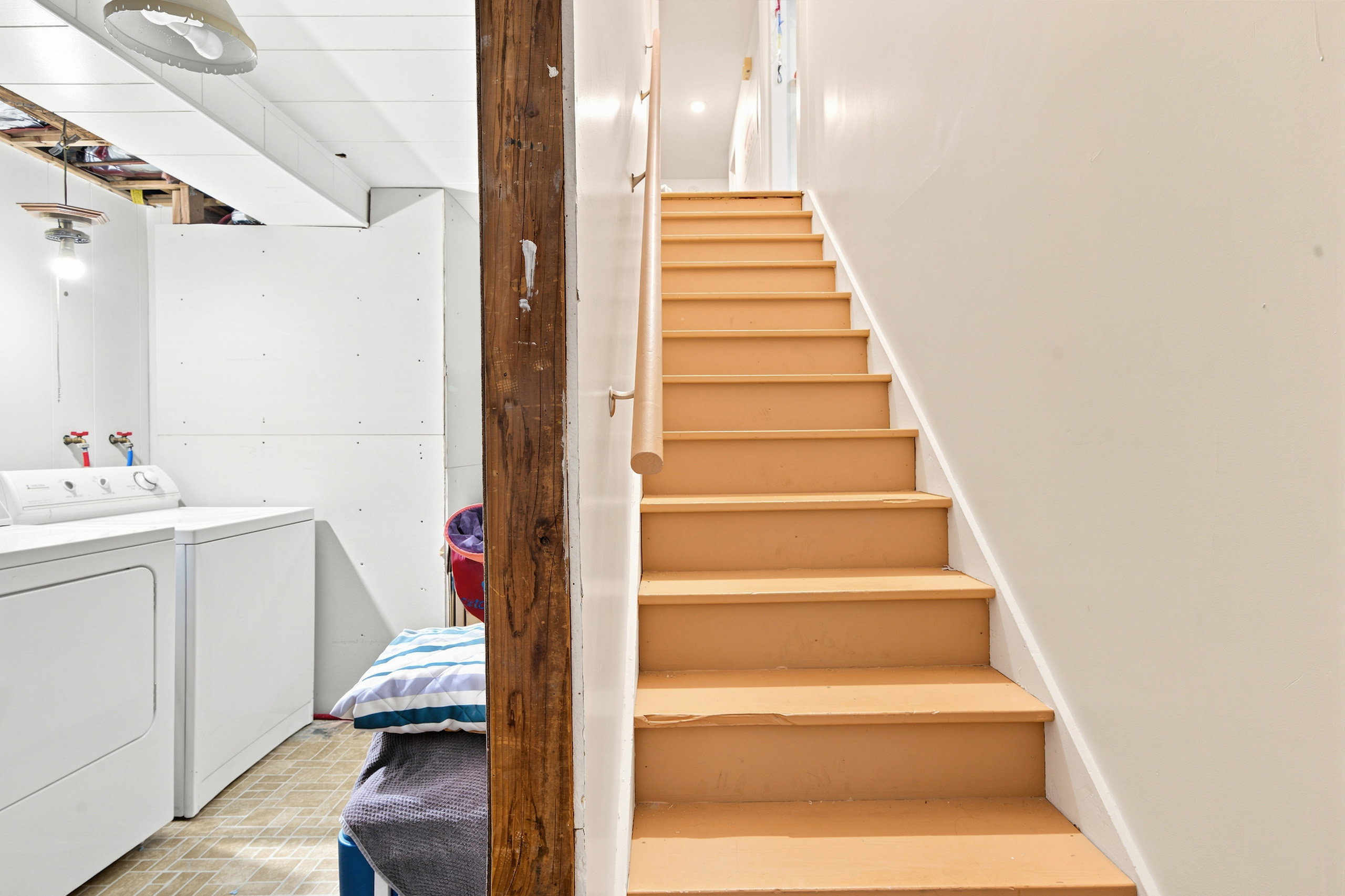 Staircase with painted treads and a natural wood handrail, featuring a prominent wood support beam