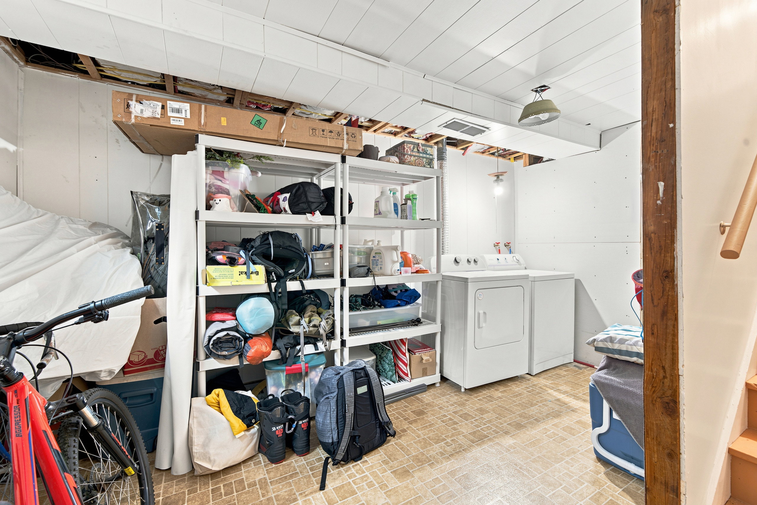 Utility area featuring a washer and dryer, exposed ceiling joists, wood-finish flooring, and a partial staircase with a wood handrail