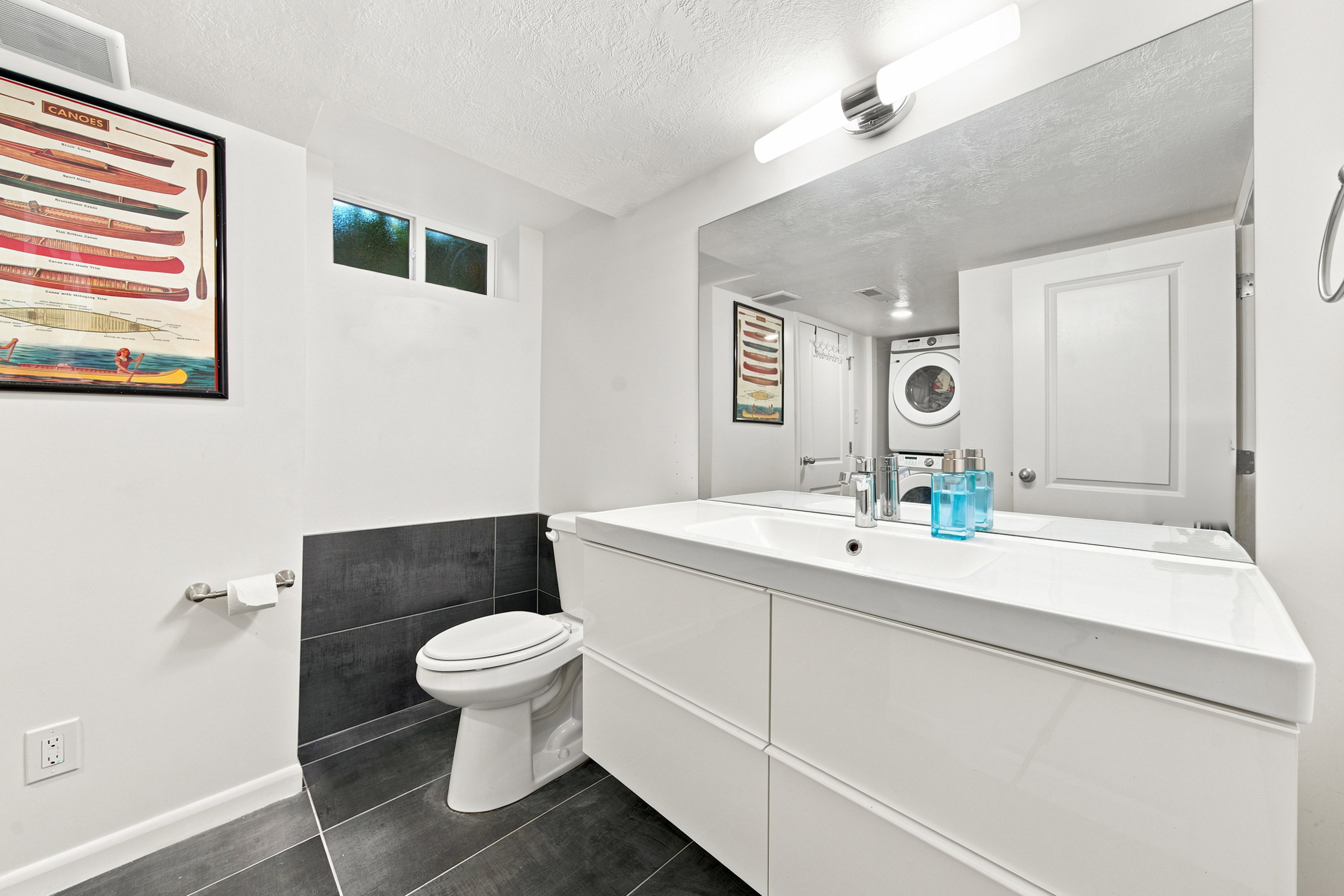 Integrated laundry appliances within a bathroom featuring a modern vanity with an integrated sink, a wall-mounted mirror, and sleek dark tile flooring