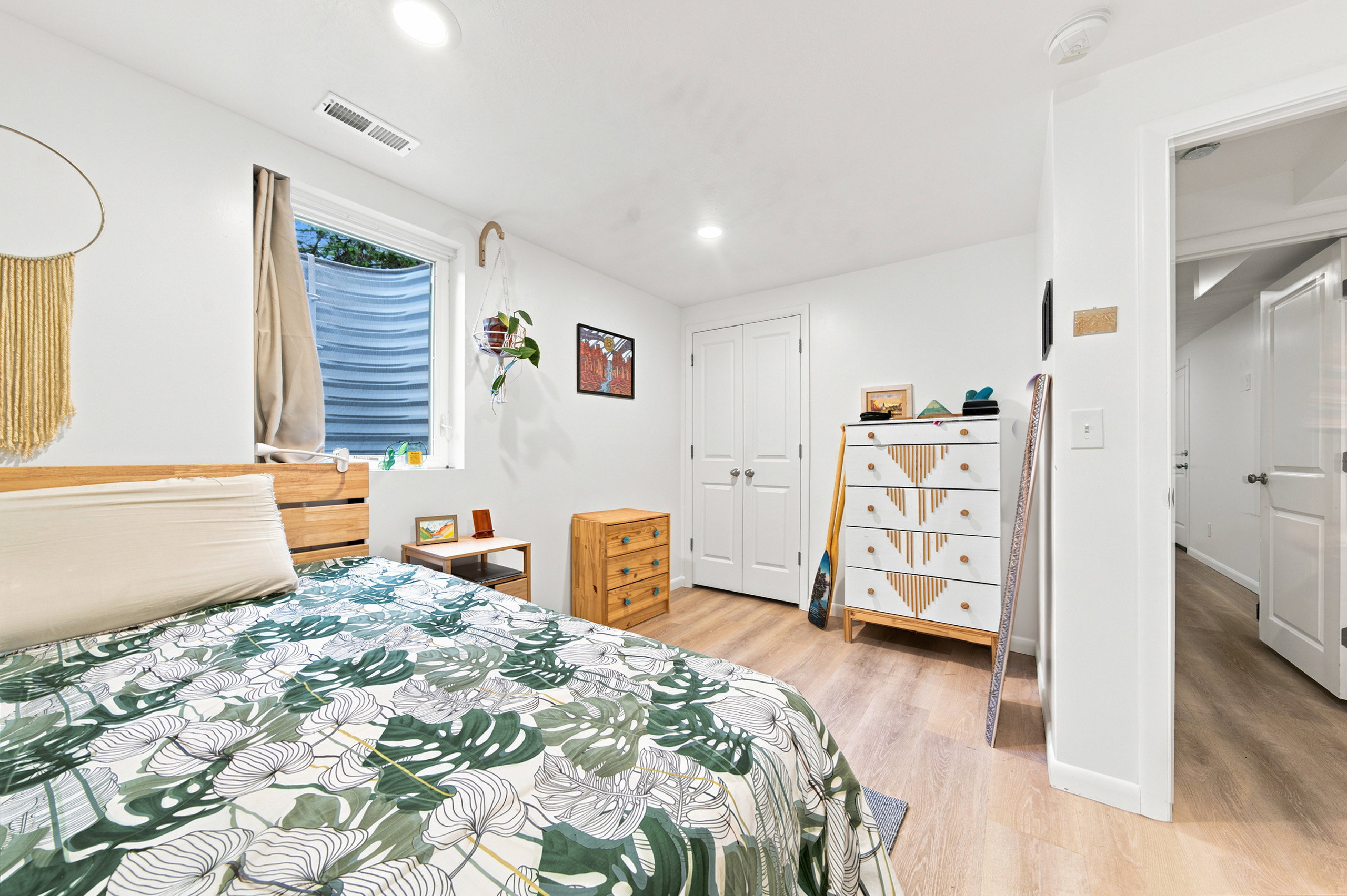 Bright bedroom featuring light wood-finish flooring, white walls, a window with a window well, and bi-fold closet doors