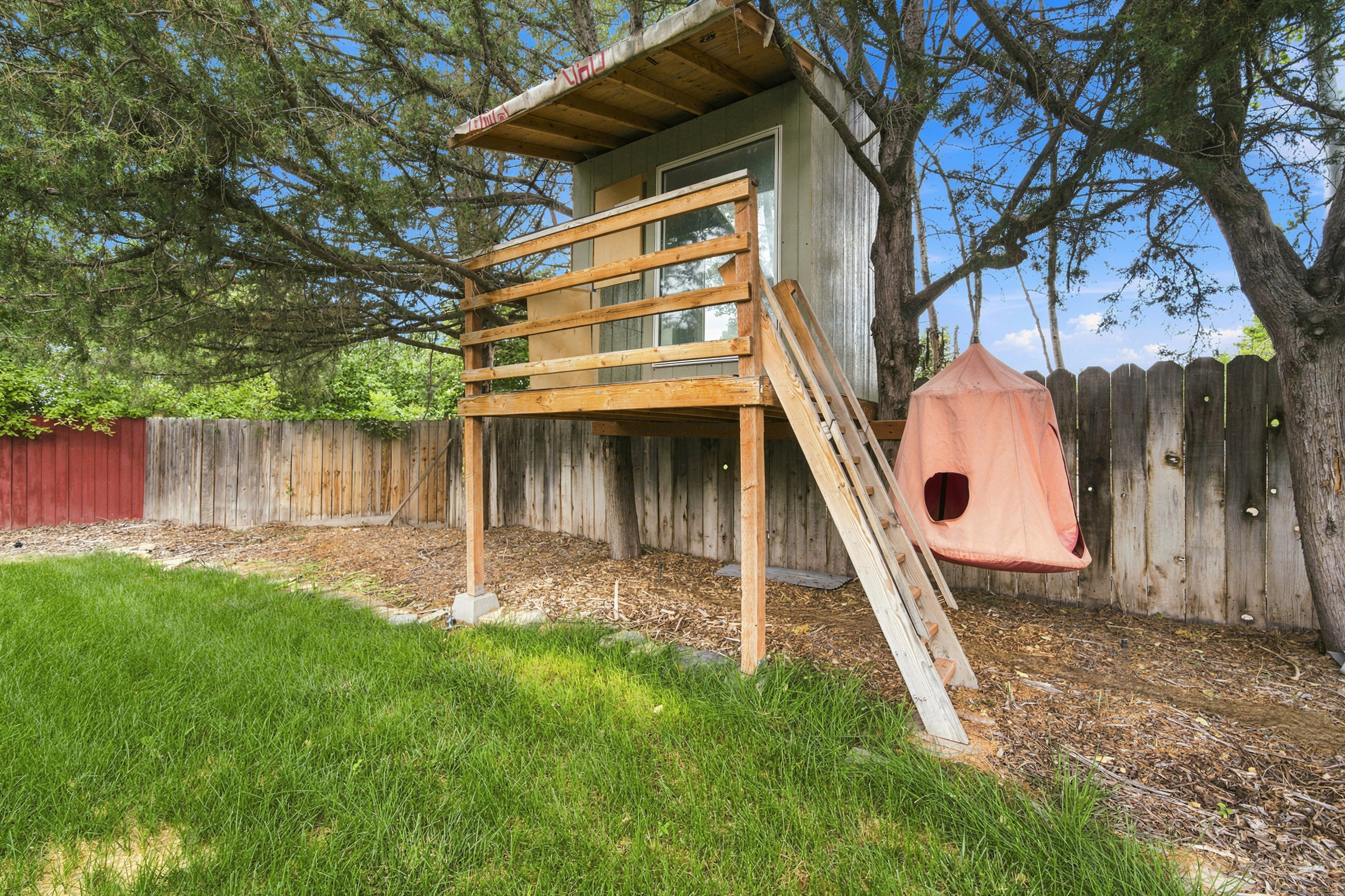 Backyard featuring a custom-built treehouse with an elevated deck, wood railing, and a window