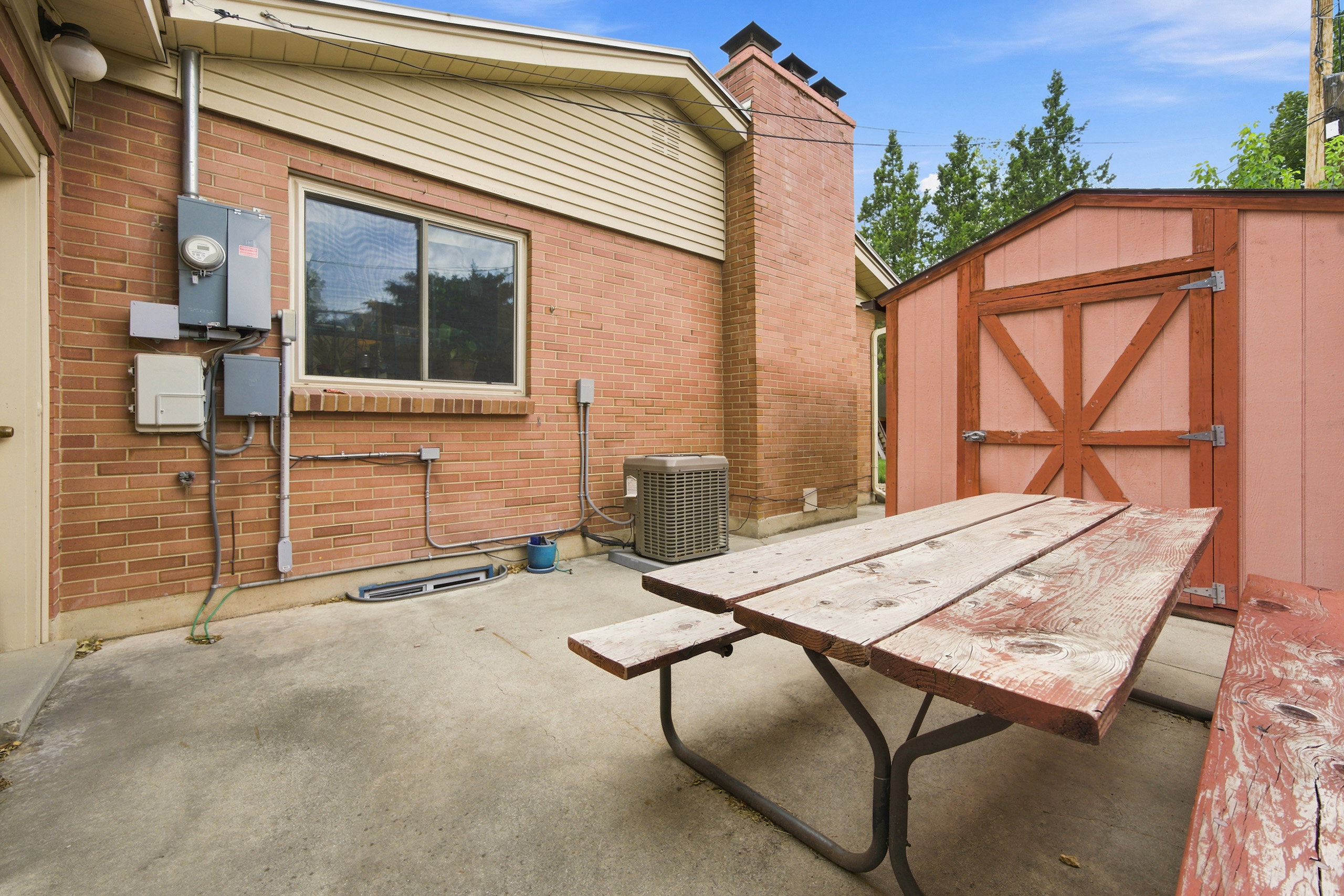 Concrete patio featuring a red brick exterior, a utility shed with a barn-style door, and an exterior window