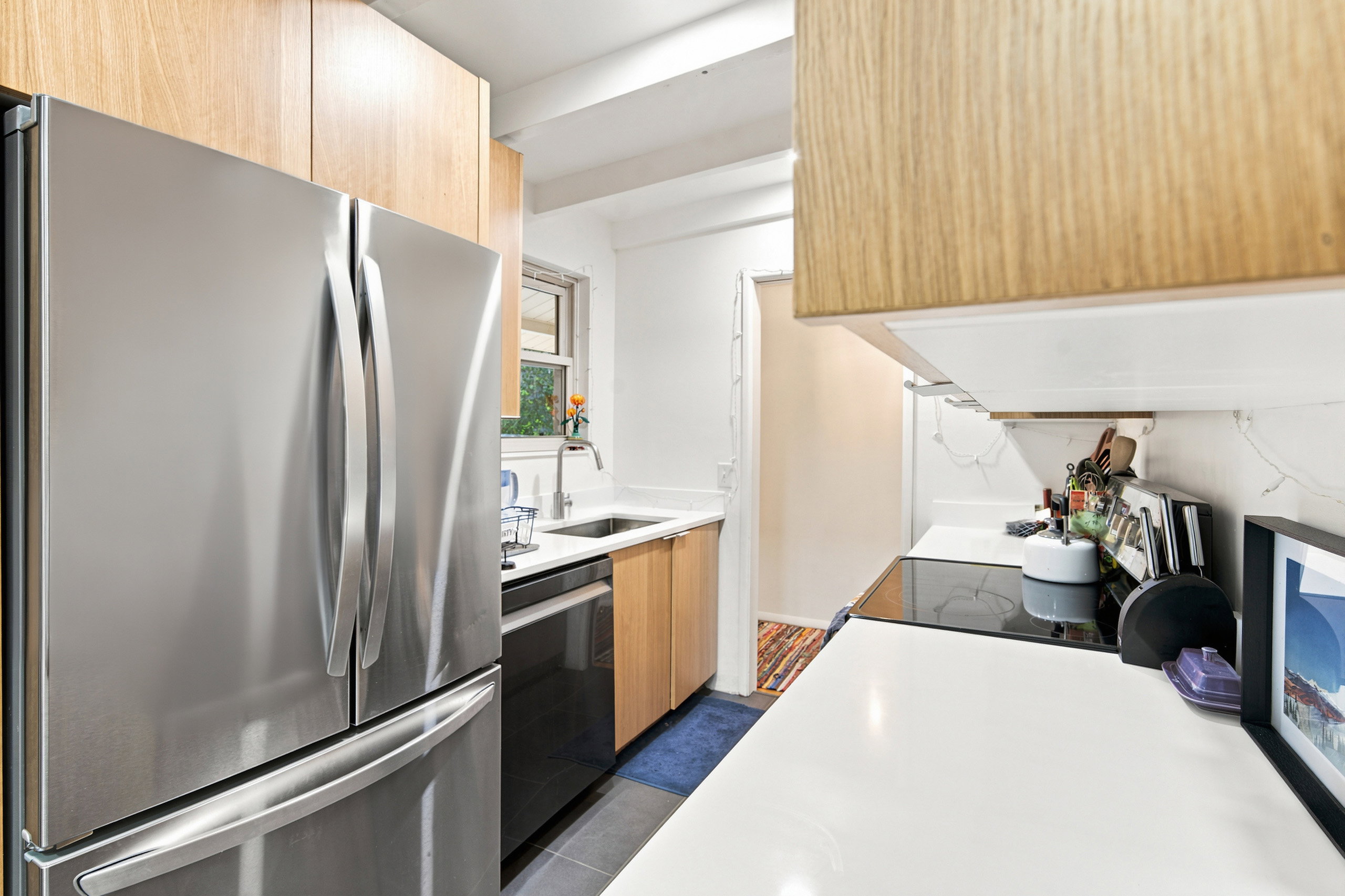 Kitchen featuring stainless steel French door refrigerator, light wood cabinetry, white countertops, and a stainless steel sink with a gooseneck faucet