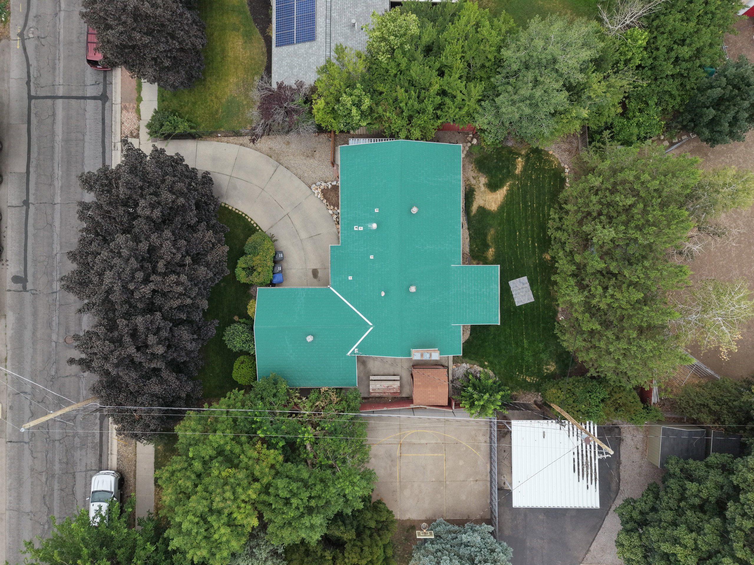 Property featuring a bright green roof, mature landscaping, paved driveway, and a spacious backyard with a basketball court