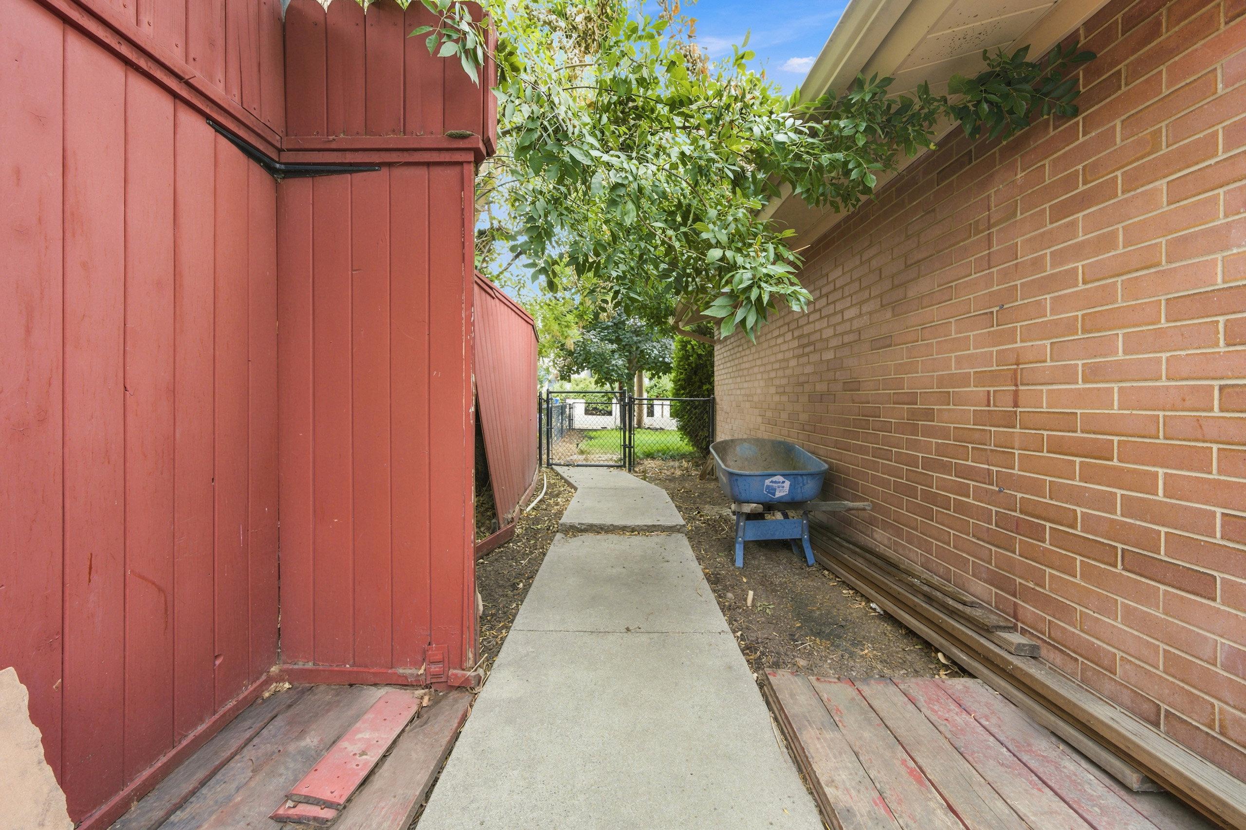 Concrete pathway extending through the property, bordered by a red board-and-batten fence and a brick wall