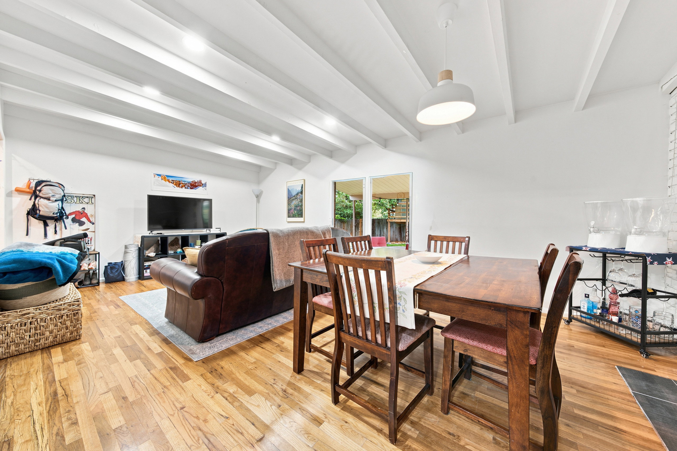 Open-concept living and dining area featuring wood-finish flooring and a vaulted ceiling with exposed white beams