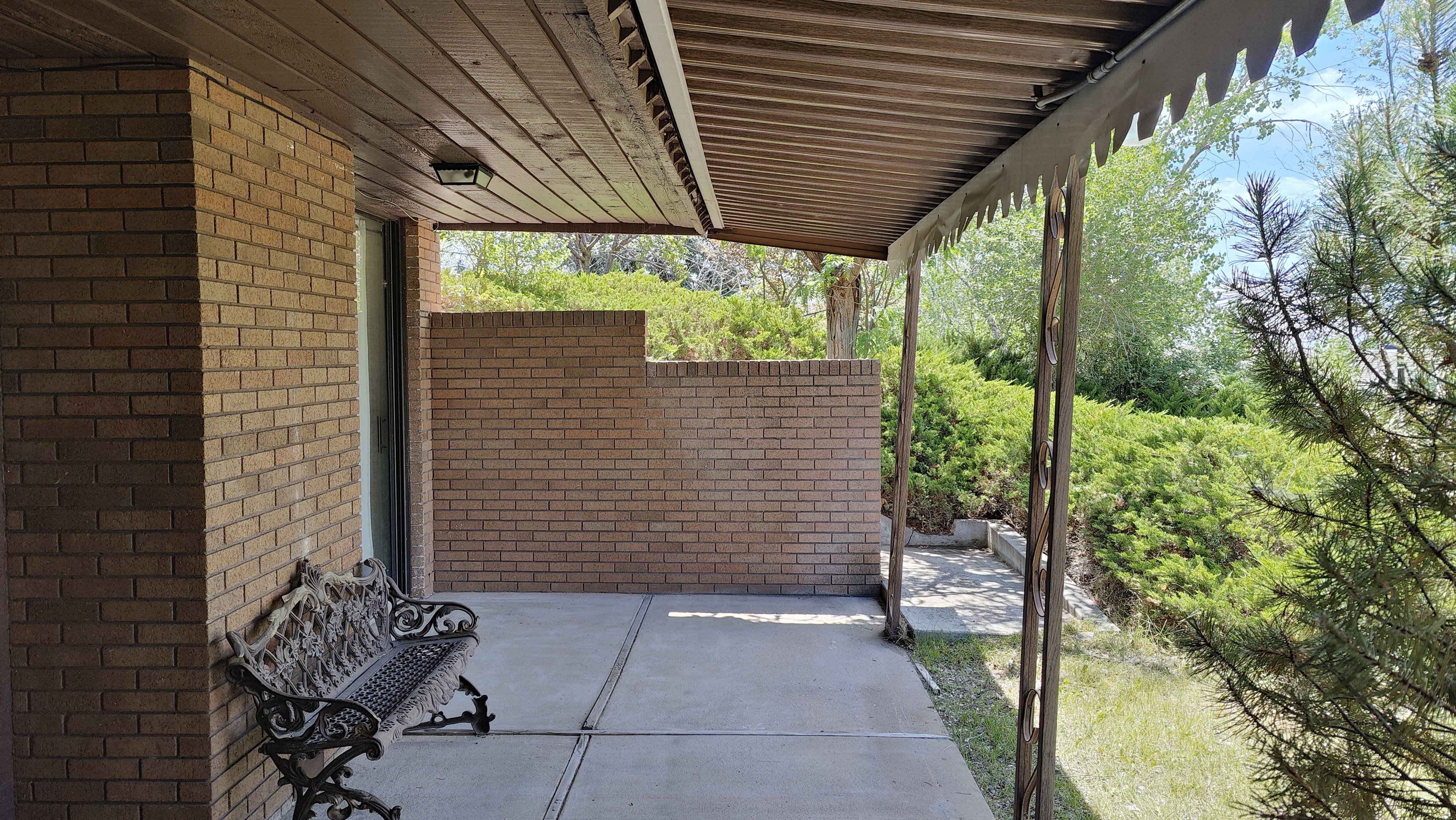 Covered brick patio featuring a wood-finish ceiling with an attached light fixture, concrete flooring, and surrounding brick walls