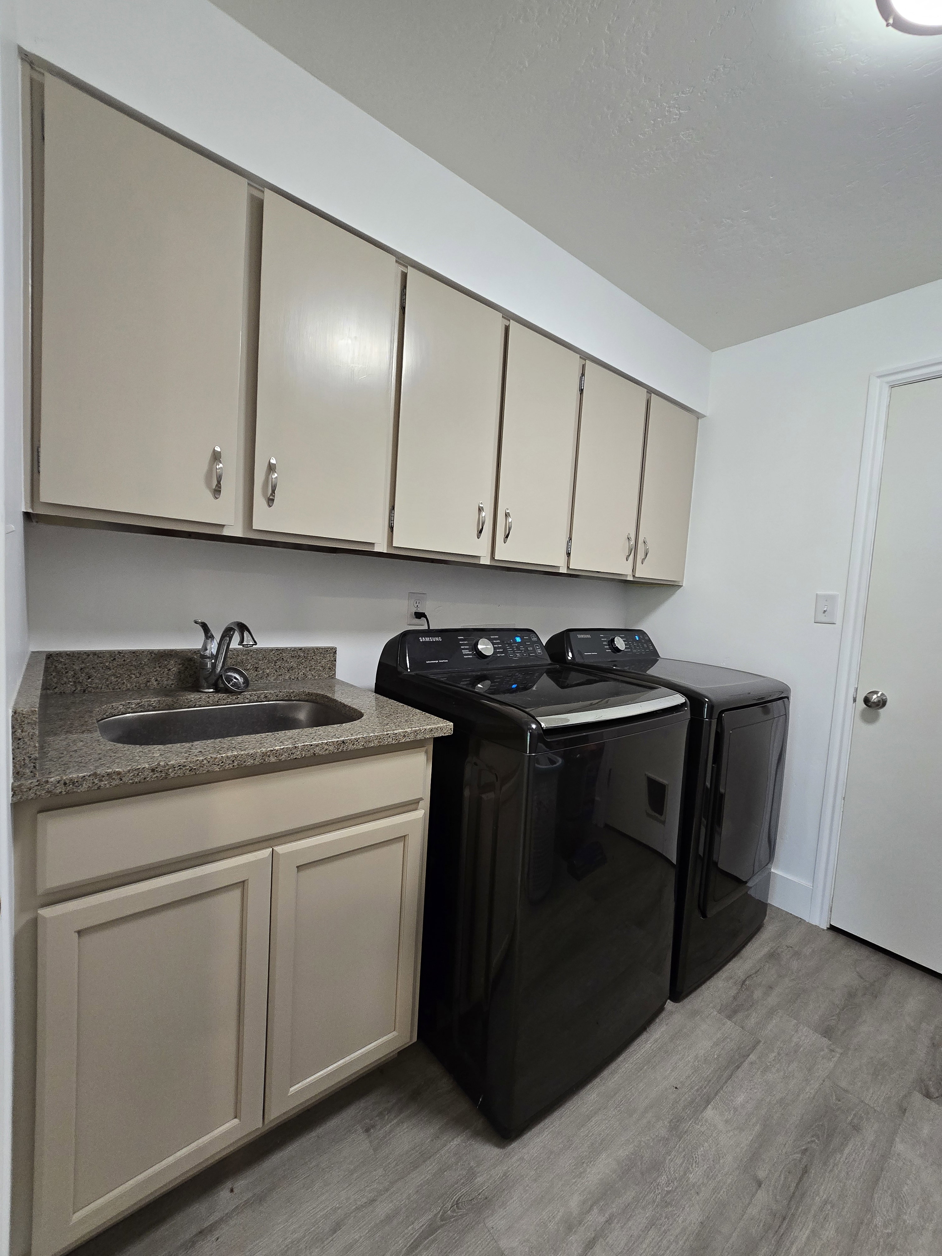 Utility area featuring ample cabinetry, a built-in sink with a stone-finish countertop, and wood-finish flooring