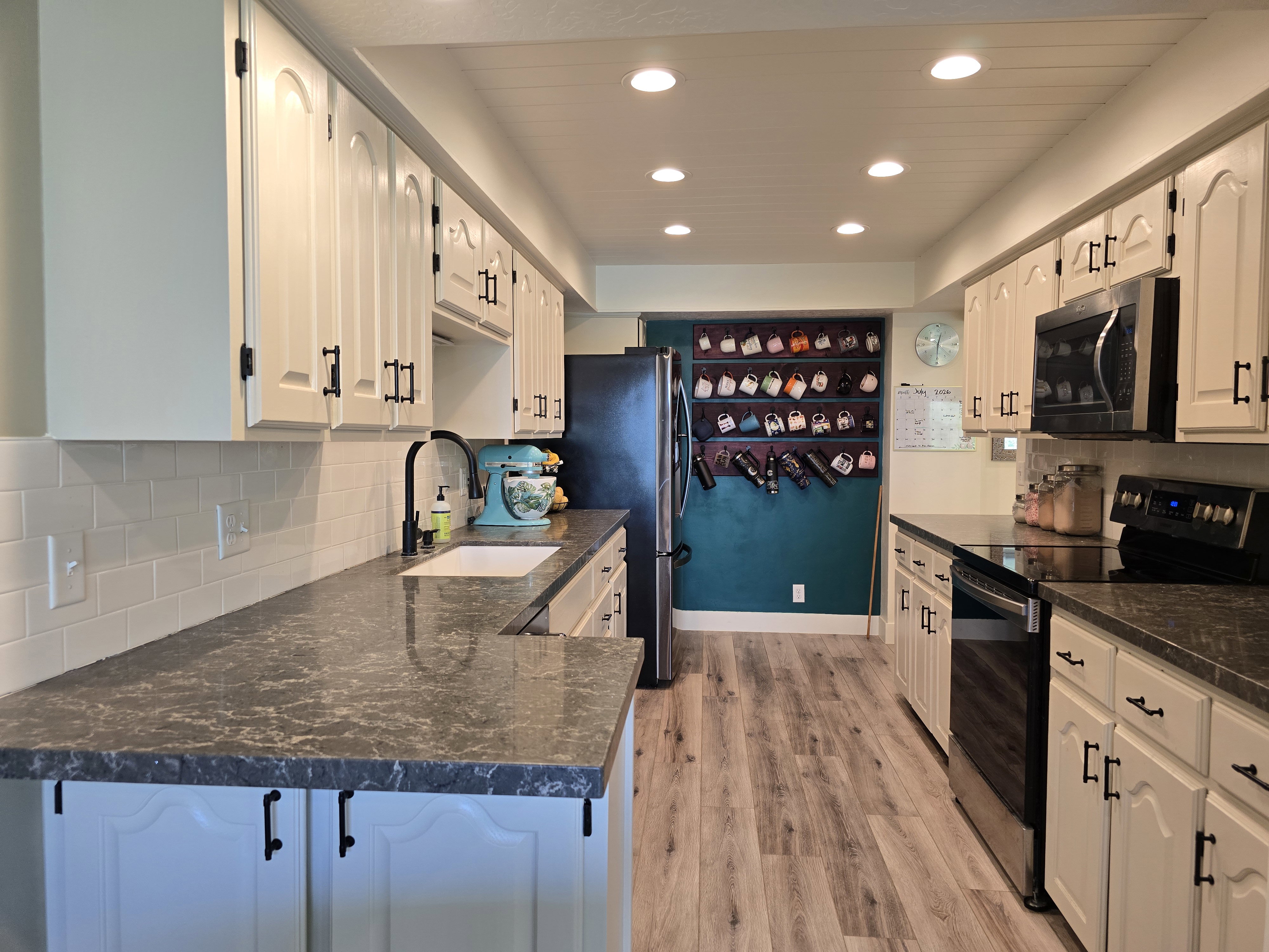 Modern kitchen featuring light-toned cabinetry with dark hardware, dark patterned countertops, and a white subway tile backsplash