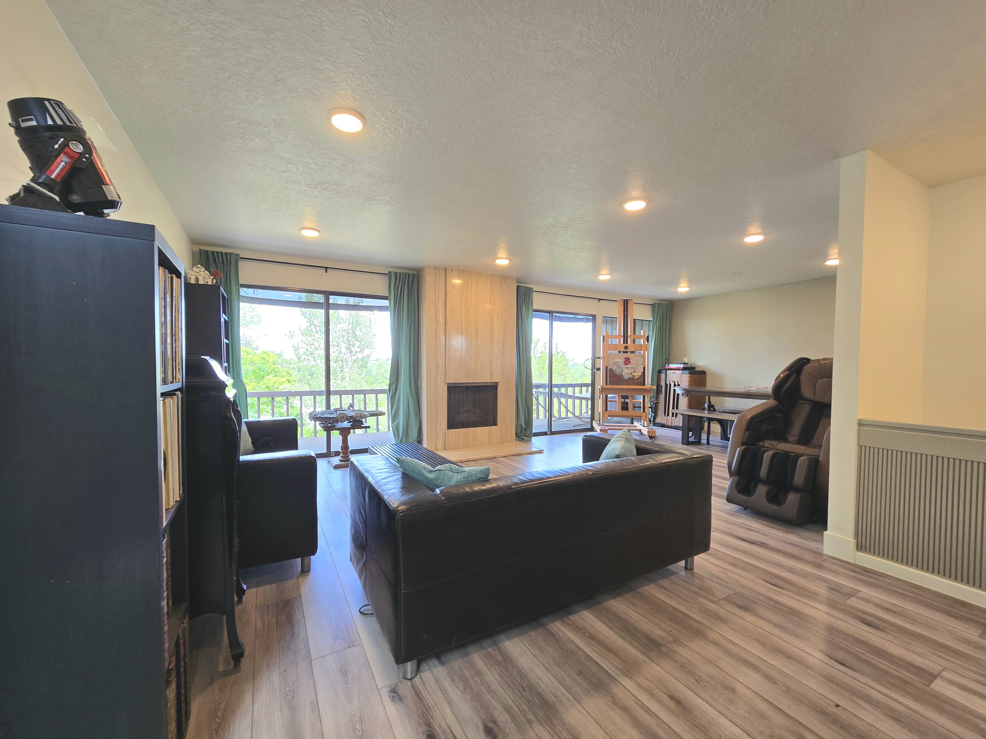 Spacious living area featuring wood-finish flooring, recessed ceiling lighting, and a fireplace with a light wood surround