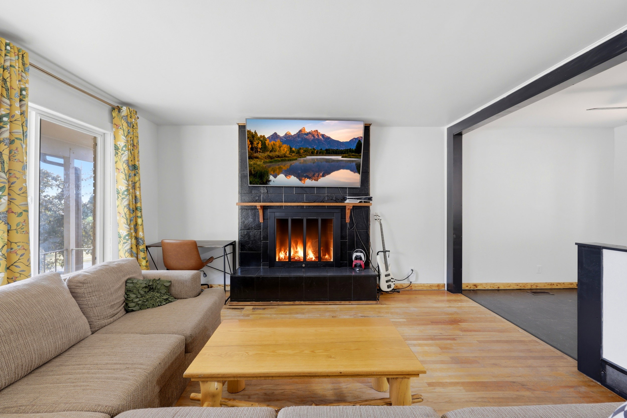Living area featuring a black tile fireplace with a wood mantle, wood-finish flooring, white walls, and a large window