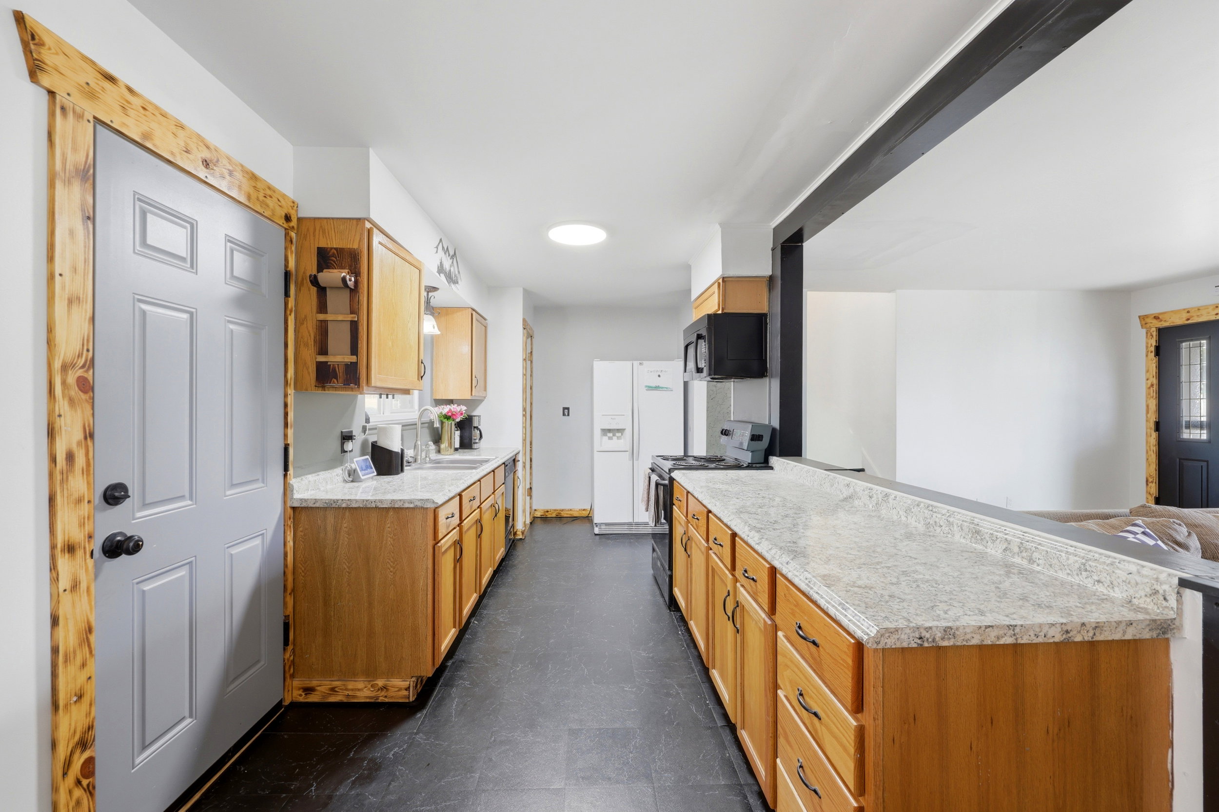 Kitchen featuring wood cabinetry, stone-finish countertops, black appliances, and dark tile flooring