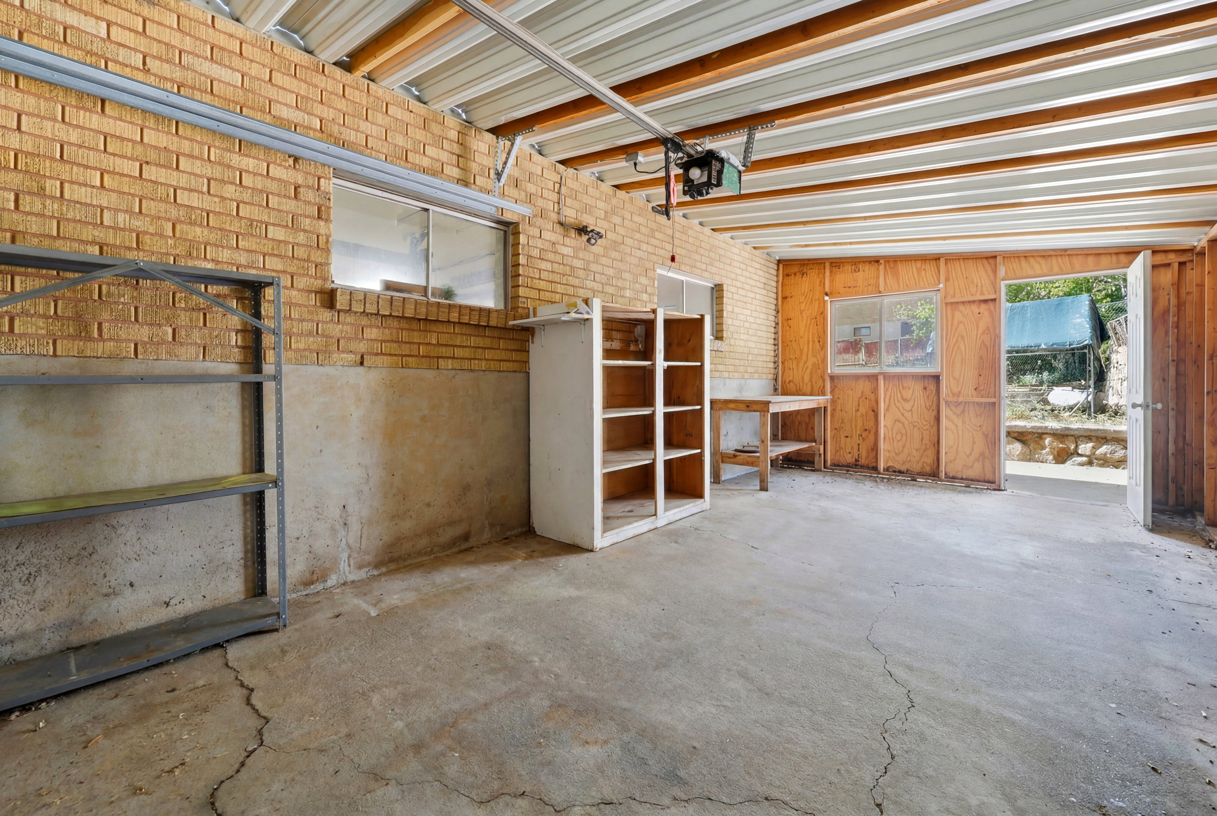 Spacious garage with exposed brick walls, concrete flooring, and an overhead garage door mechanism
