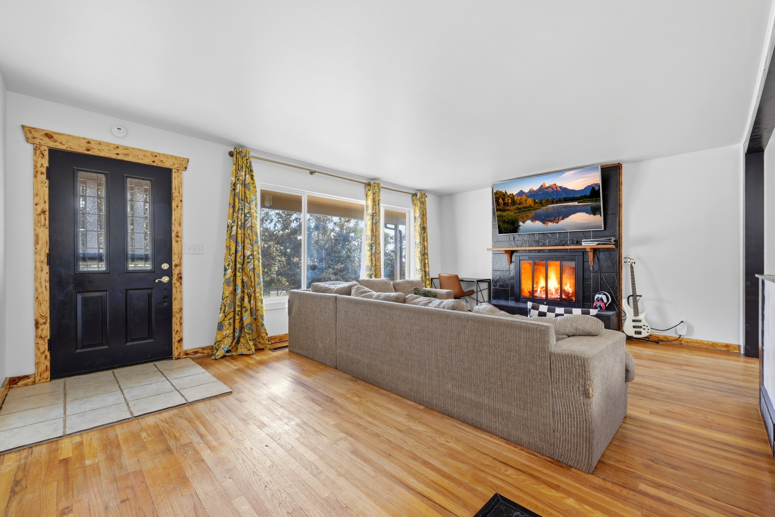 Spacious living area featuring polished wood-finish flooring, a black tiled fireplace with a wood mantle, and a large picture window