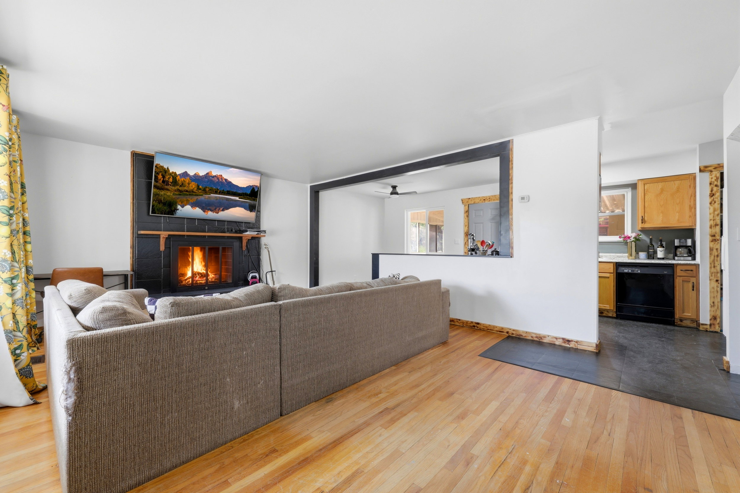 Living space featuring wood-finish flooring, a black tiled fireplace with a mantel, and an open pass-through window with a dark trim