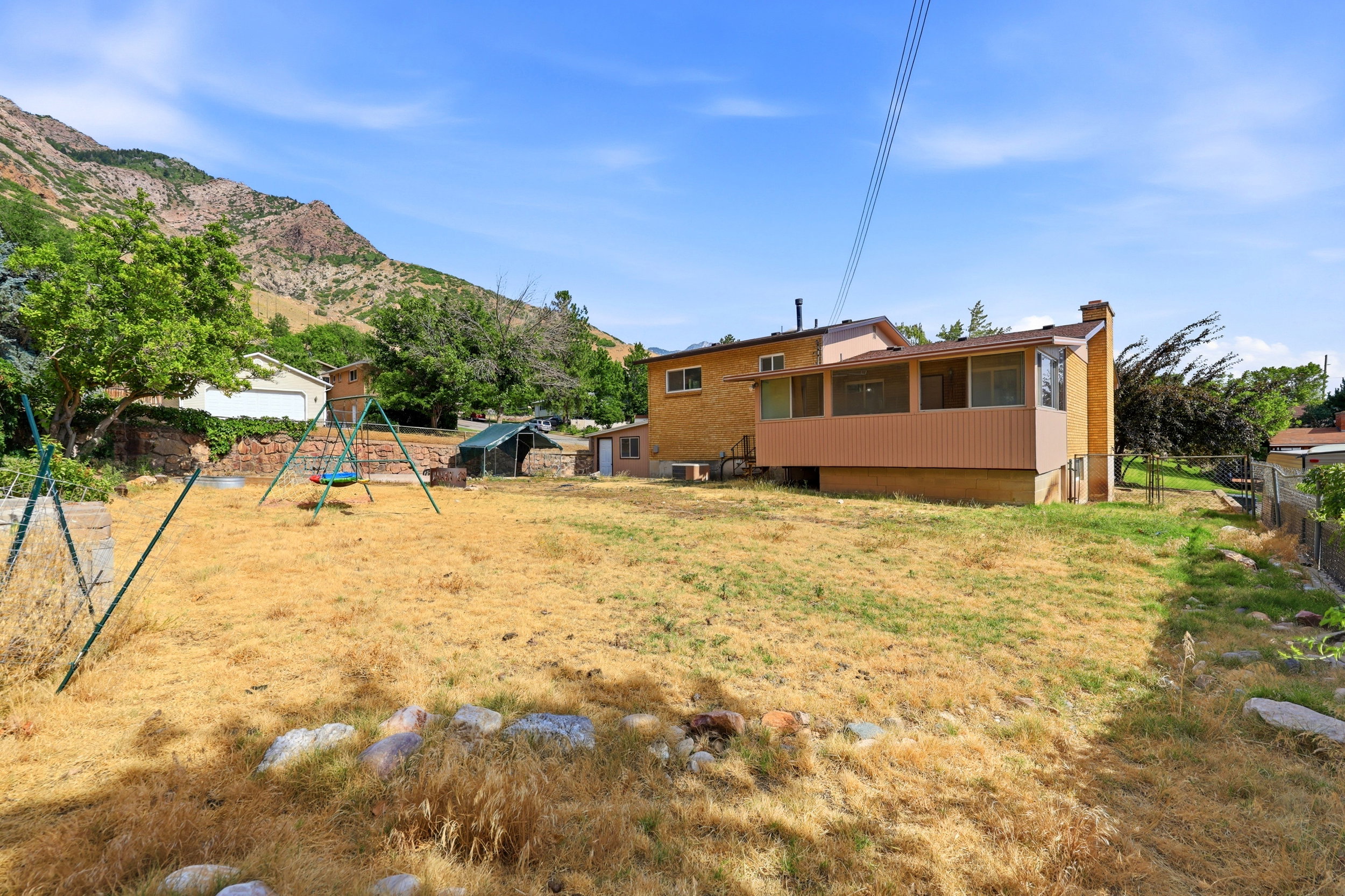 Spacious backyard featuring an elevated enclosed patio, brick exterior, and a prominent mountainous backdrop