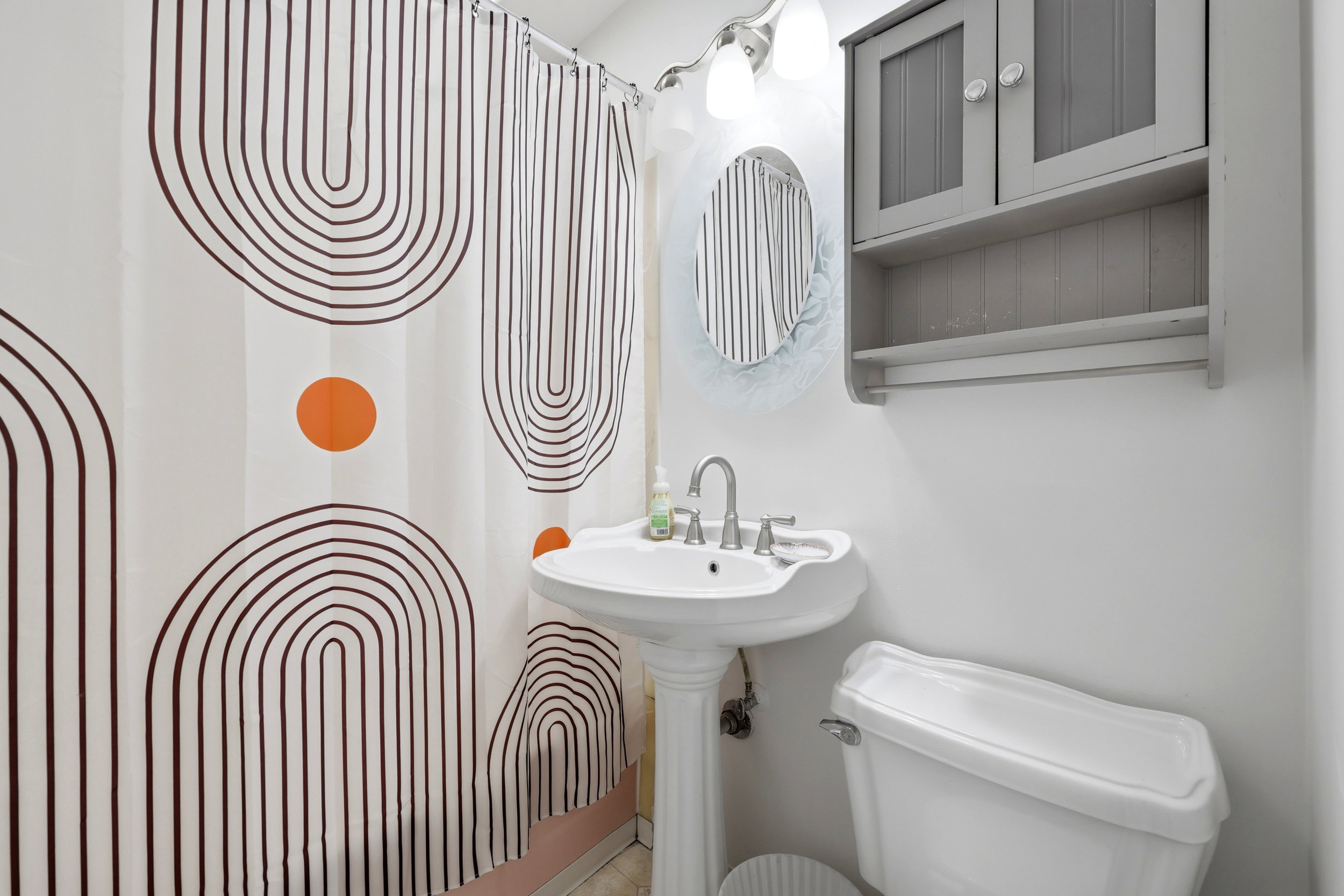 Pedestal sink with chrome faucet, wall-mounted storage cabinet, and white toilet