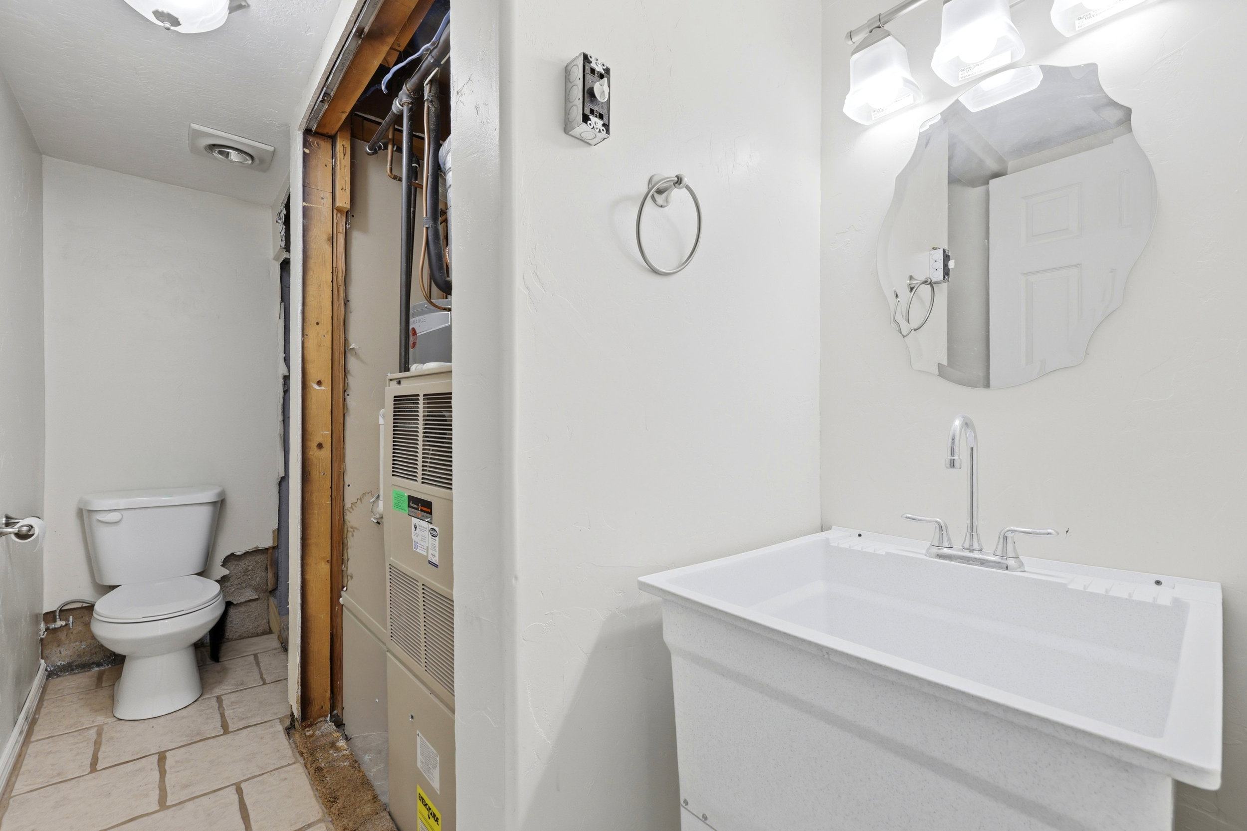 Utility sink with a chrome faucet, illuminated by a three-bulb vanity light fixture