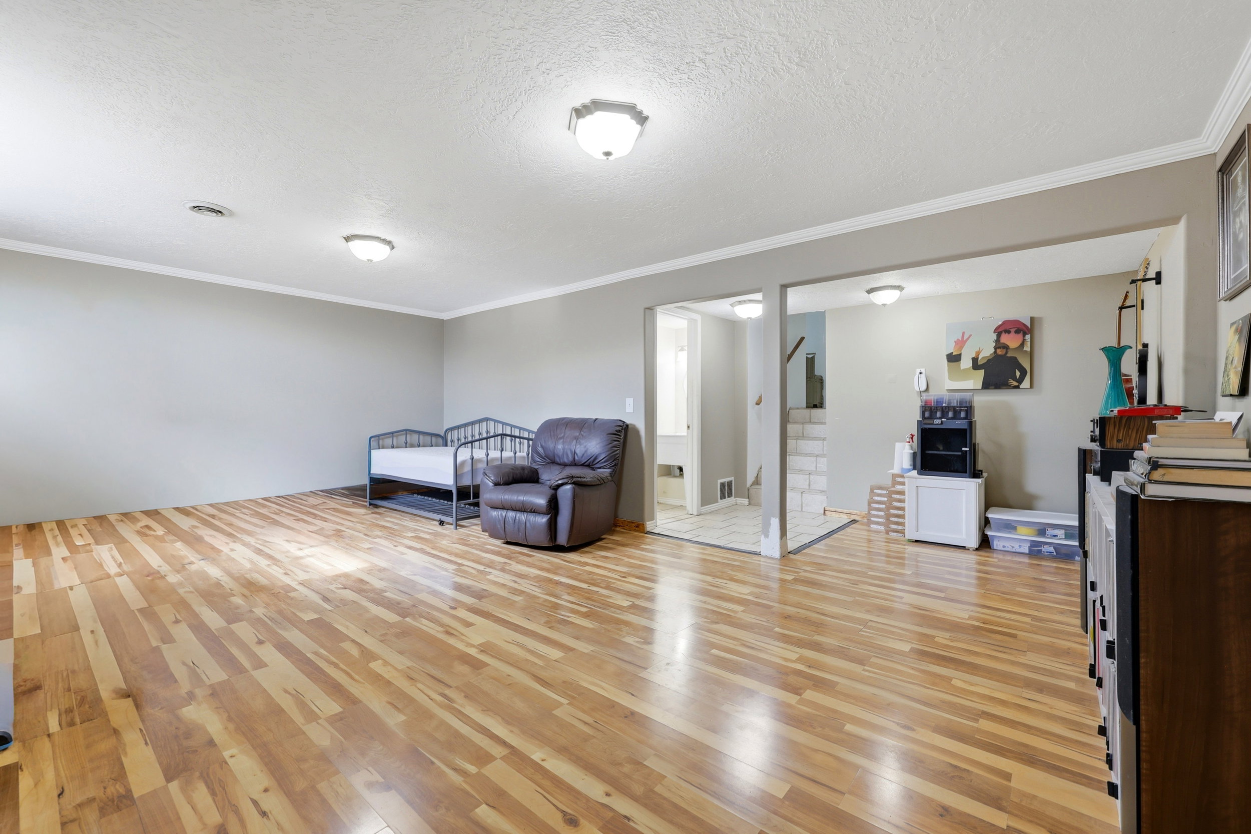 Spacious room featuring wood-finish flooring, light gray wall paint, white crown molding, and two ceiling-mounted light fixtures