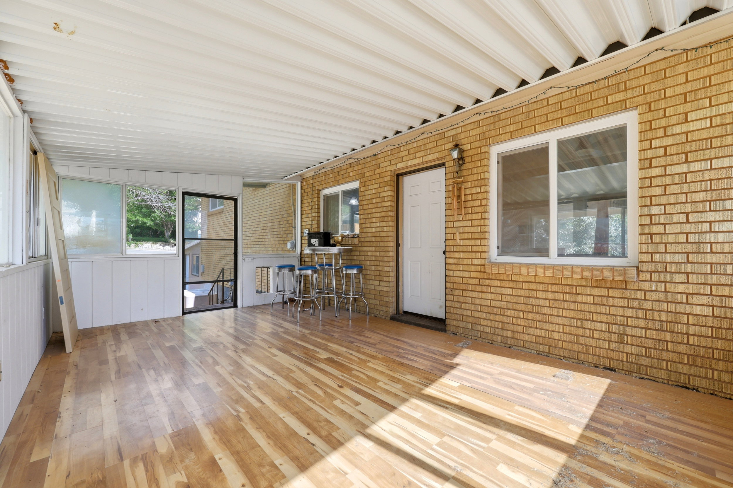 Enclosed porch with wood-finish flooring, white paneled walls, and a corrugated ceiling