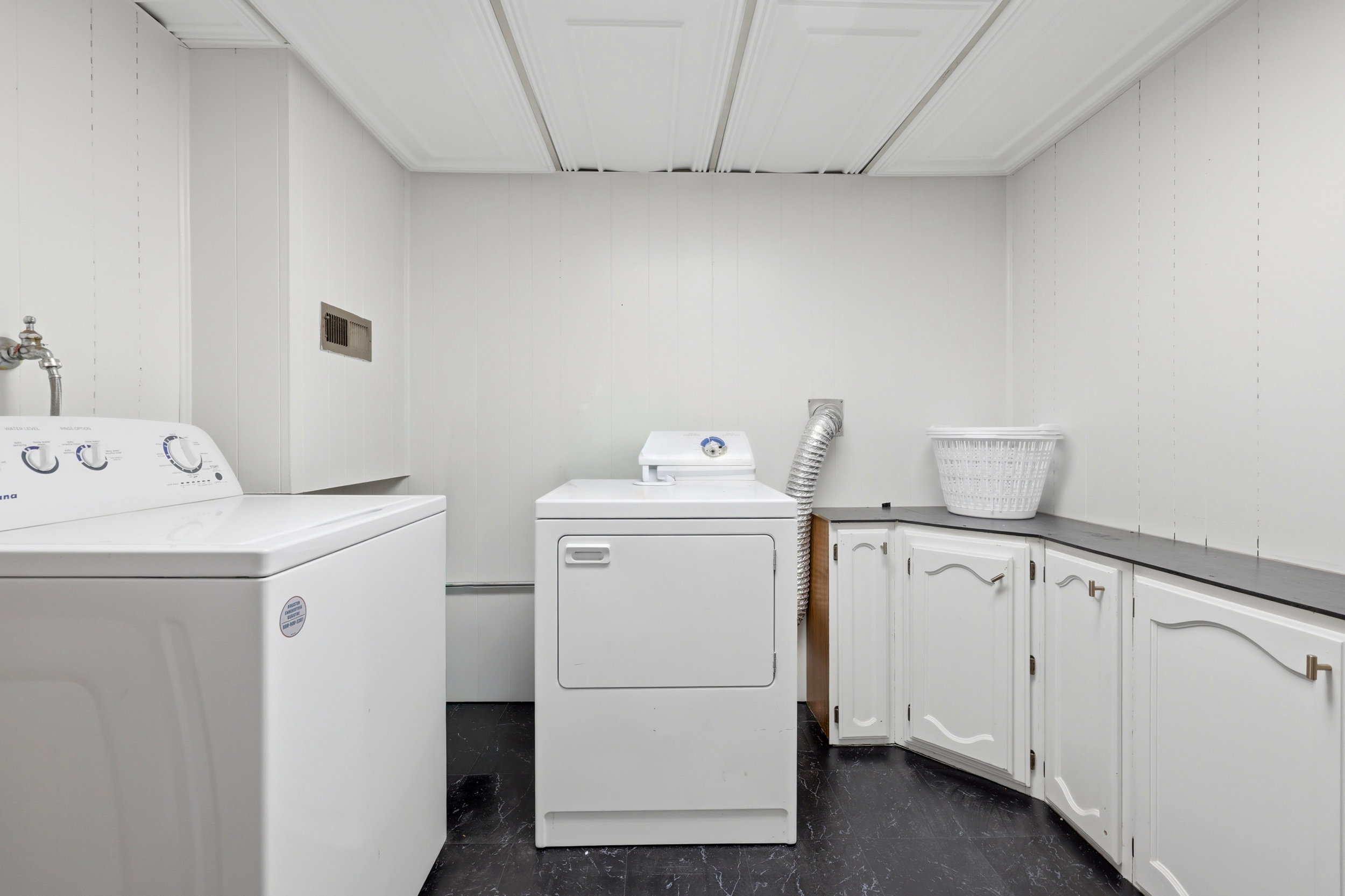 Dedicated laundry area featuring a washer and dryer, white paneling, built-in white cabinetry, a dark countertop, and dark flooring