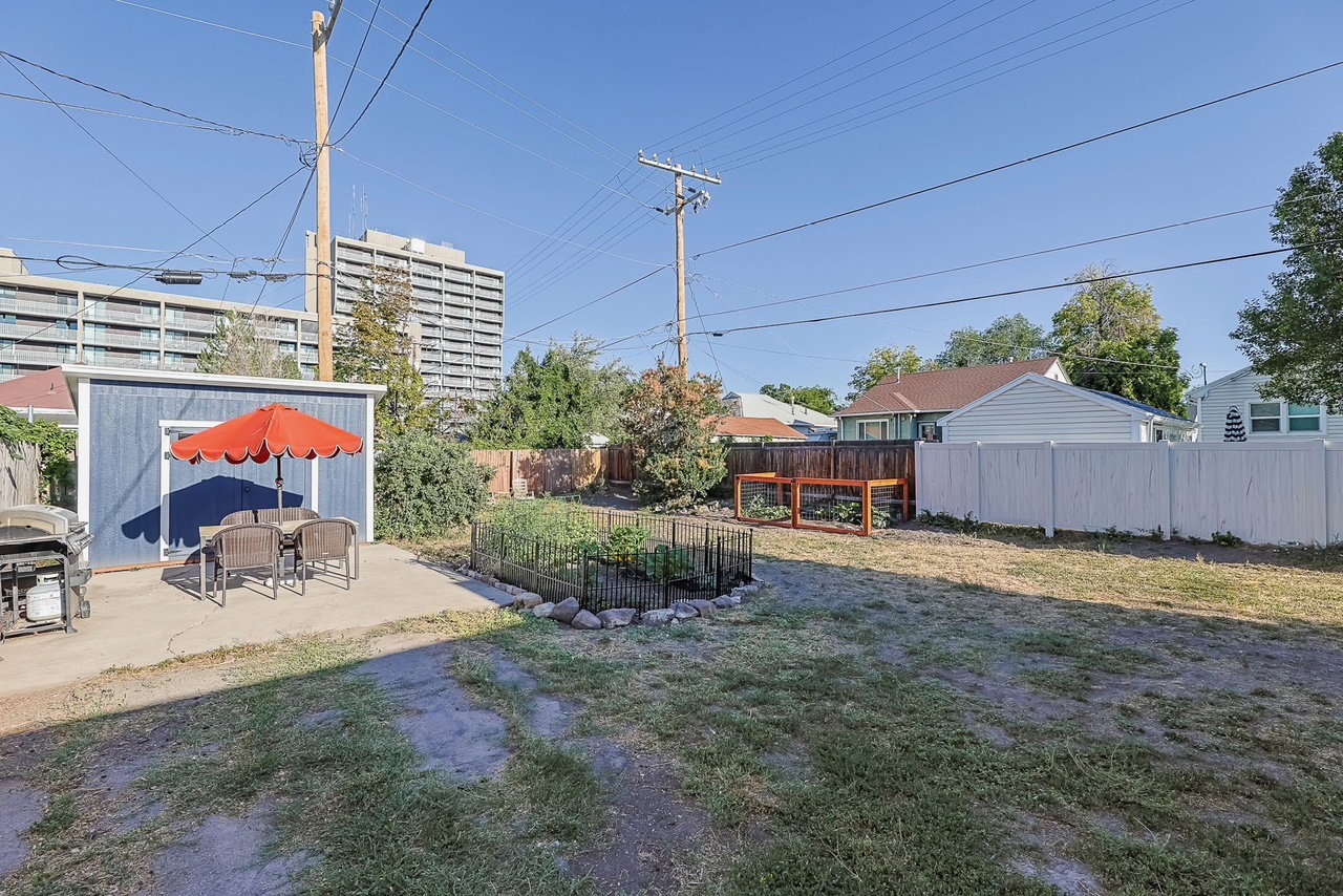 Expansive backyard featuring a concrete patio, a blue storage shed, a fenced garden area, and a white privacy fence